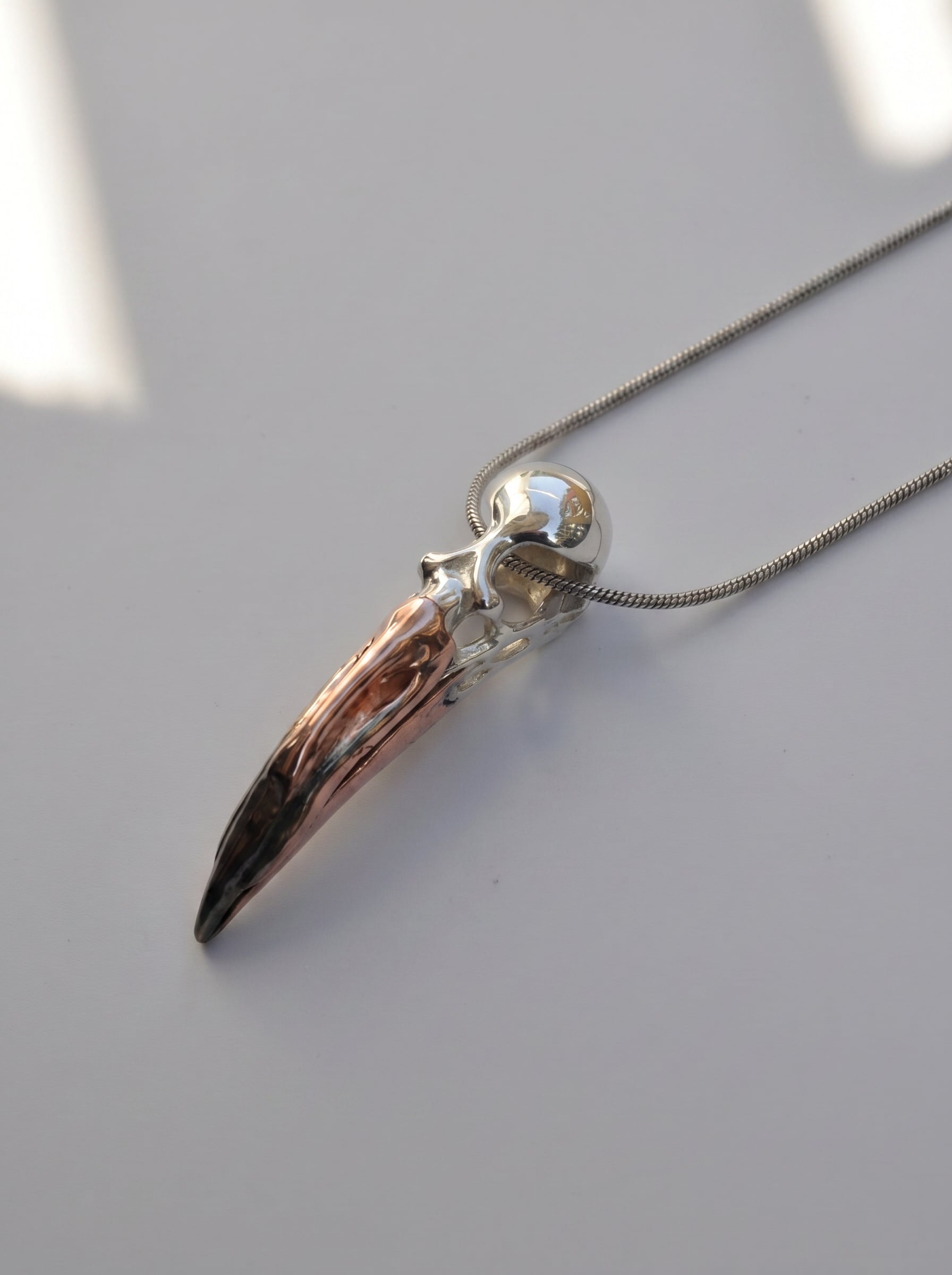 Flamingo Skull Pendant photographed flat on neutral surface, showing elongated form and mixed‑metal palette.