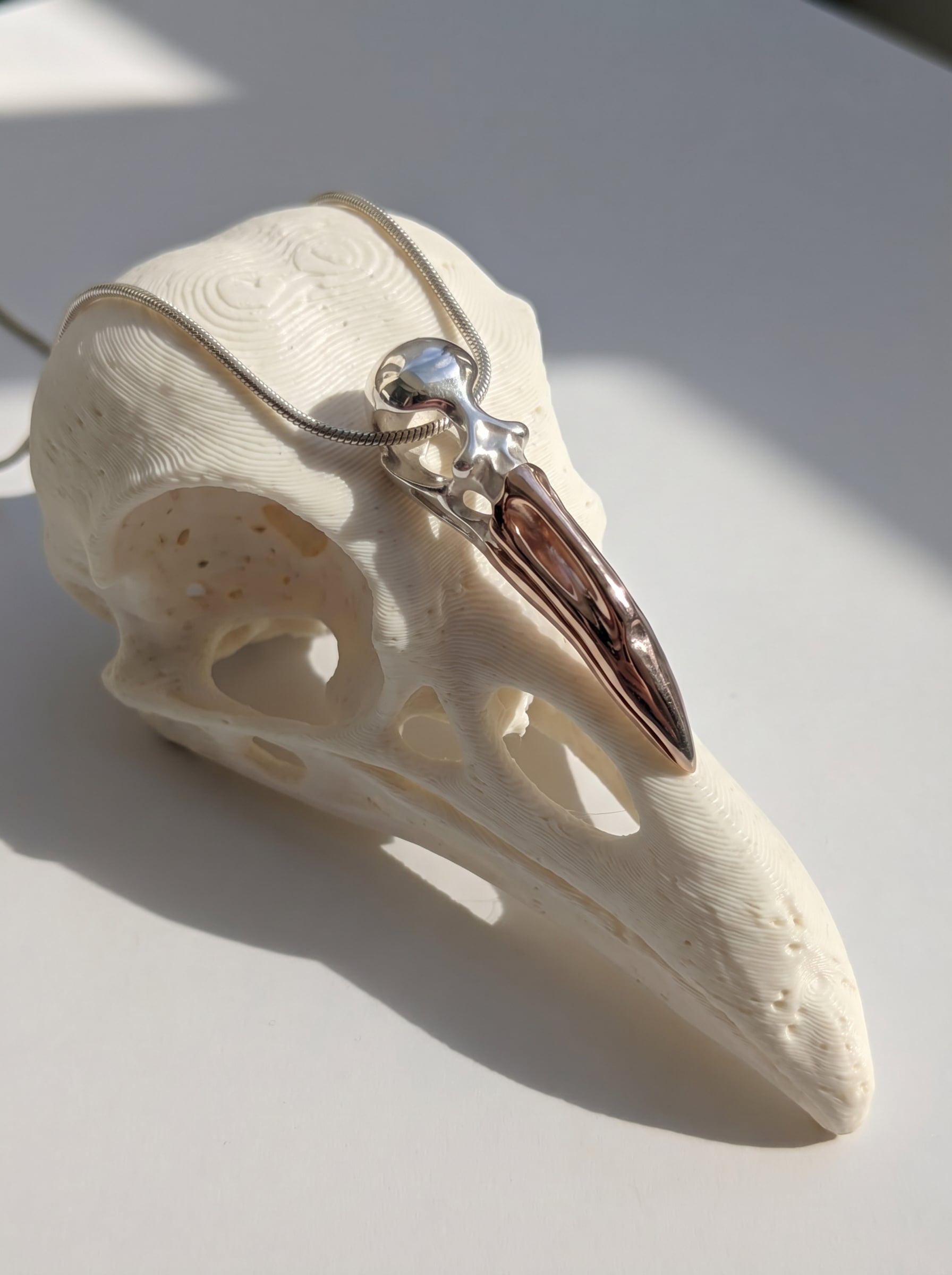 Flamingo Skull Pendant resting on sculptural display, emphasizing smooth silver contours and rose‑gold warmth.