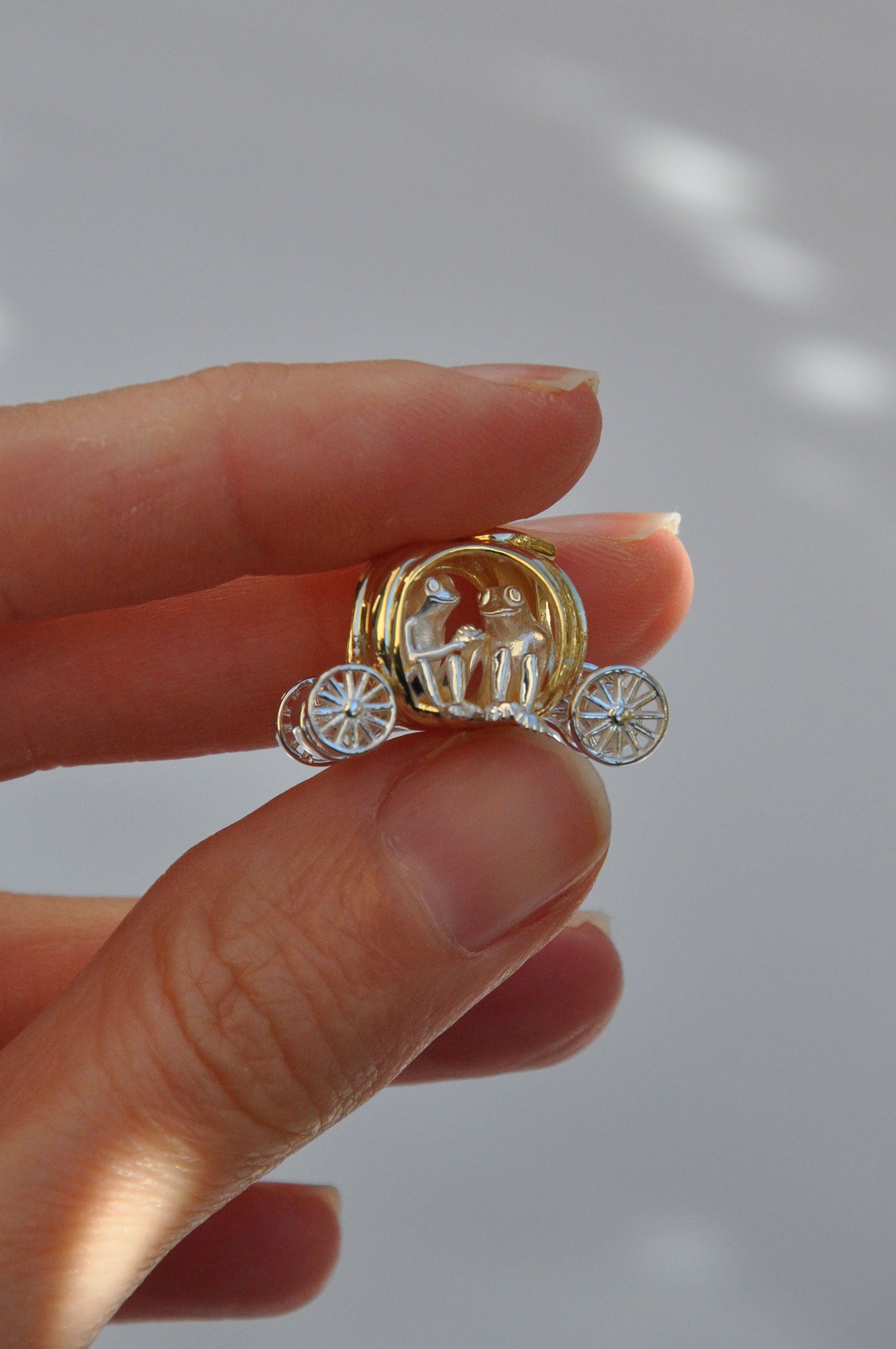 Frogs in Pumpkin Carriage Pendant held in hand, showing a miniature pumpkin carriage with sculptural frogs and freely spinning wheels