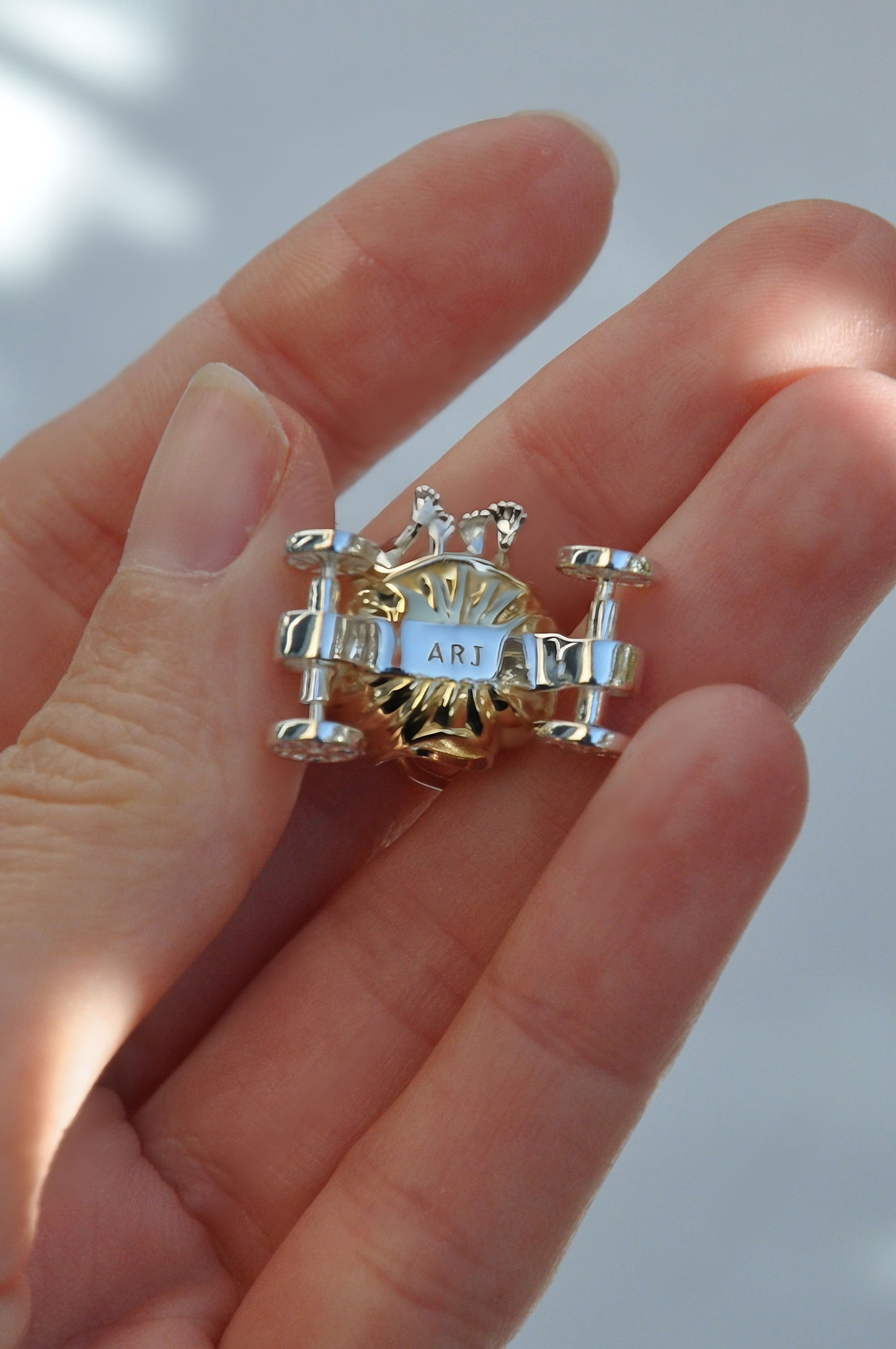 Hand holding the Frogs in Pumpkin Carriage Pendant, highlighting the gold pumpkin, silver frogs, and freely spinning wheels.