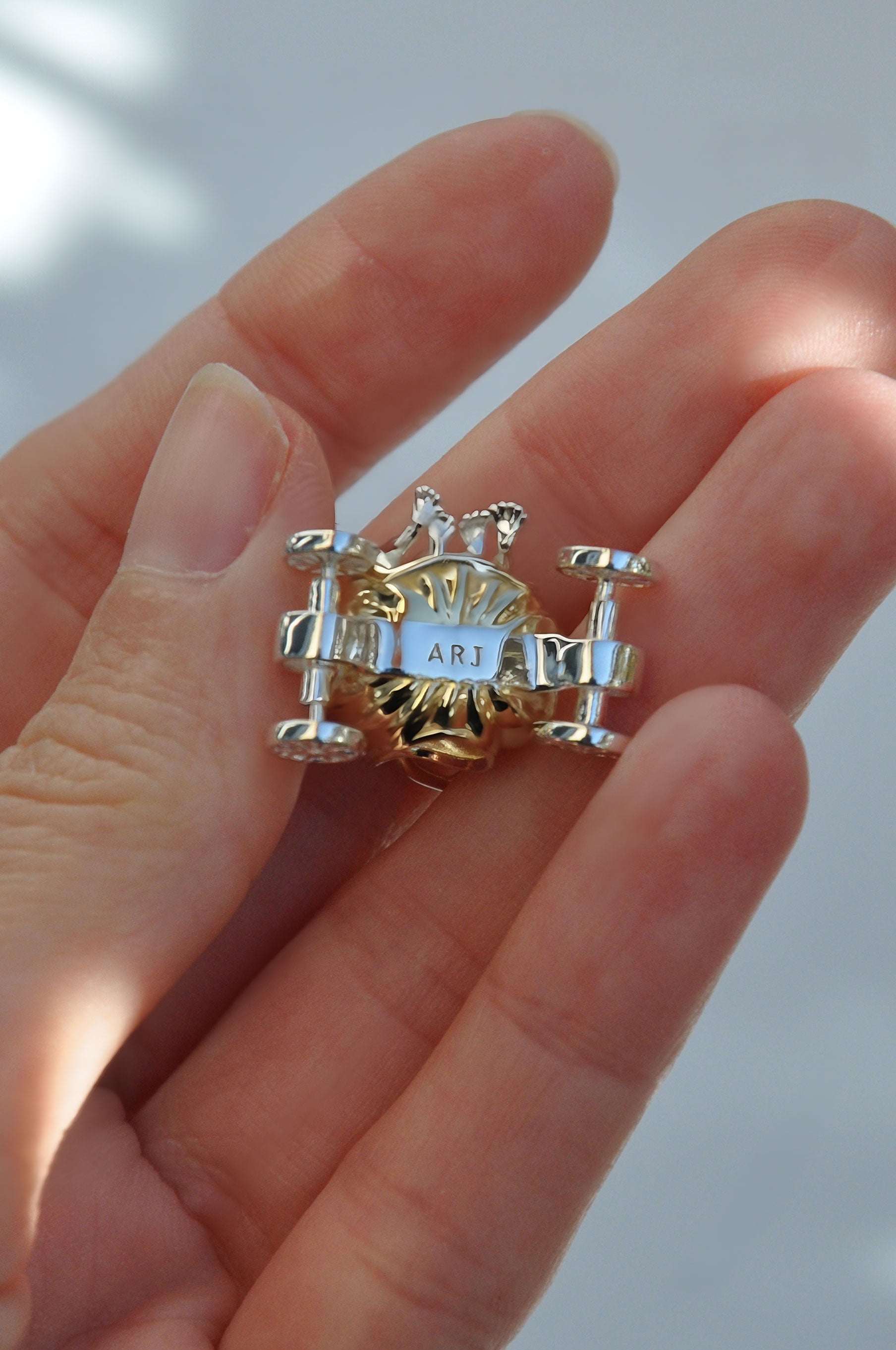 Hand holding the Frogs in Pumpkin Carriage Pendant, highlighting the gold pumpkin, silver frogs, and freely spinning wheels.