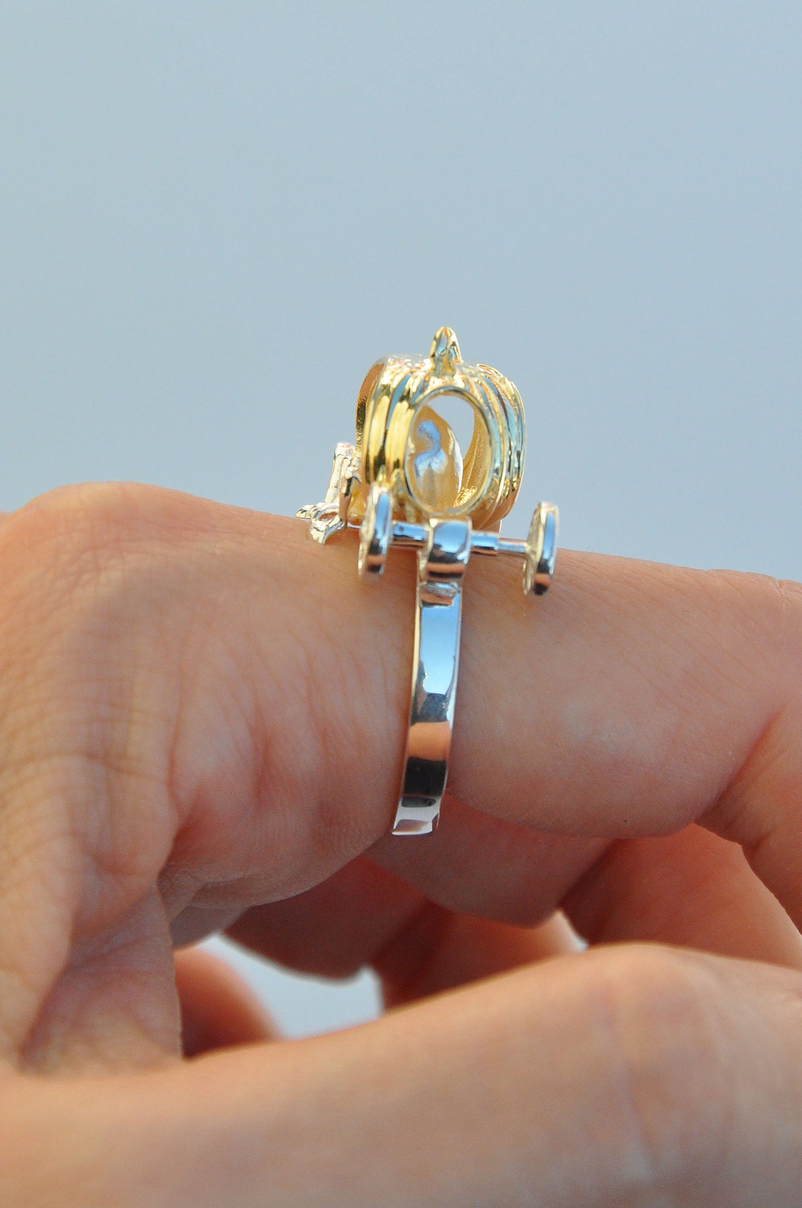 Frogs in Pumpkin Carriage Ring worn on a finger, featuring a gold pumpkin carriage with two miniature frogs seated hand‑in‑hand inside.