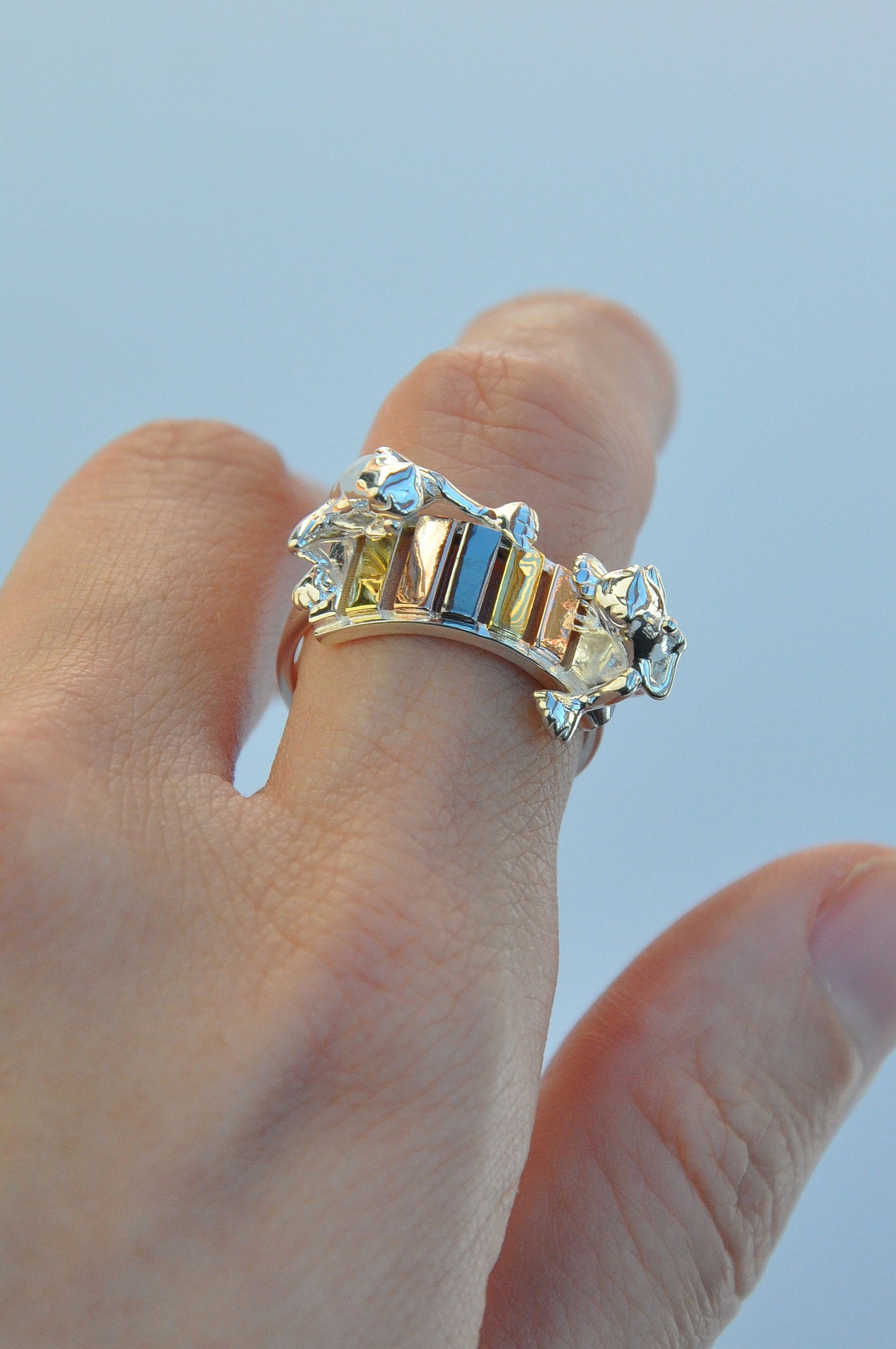 Frogs on the Rainbow Keys Ring worn on a finger, showing two tiny silver frogs and rainbow‑plated xylophone keys as a miniature wearable sculpture