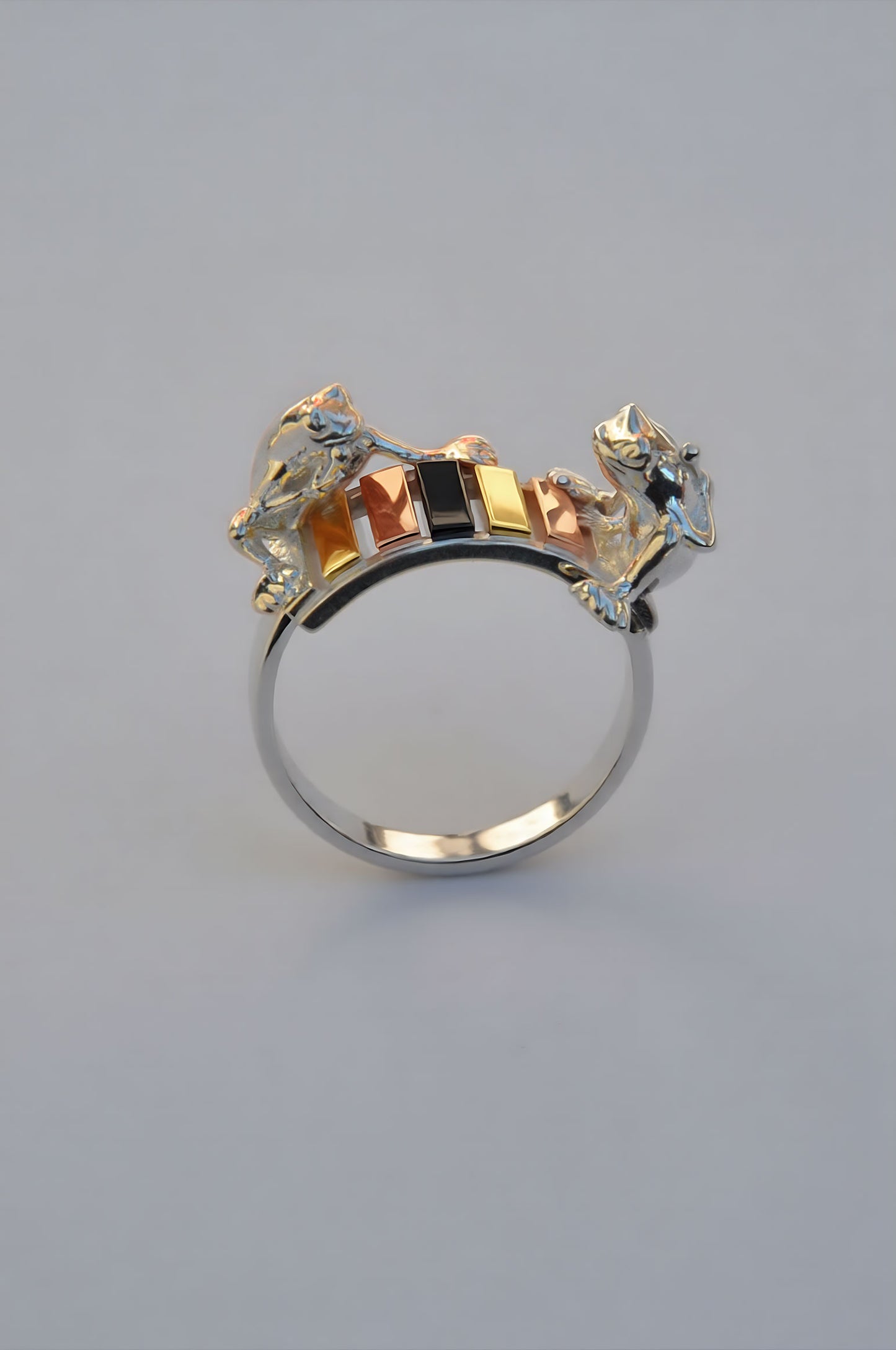 Frogs on the Rainbow Keys Ring featuring two sculpted silver frogs perched on a miniature xylophone with rainbow‑plated keys in 14k gold, rose gold, black rhodium, and sterling silver.