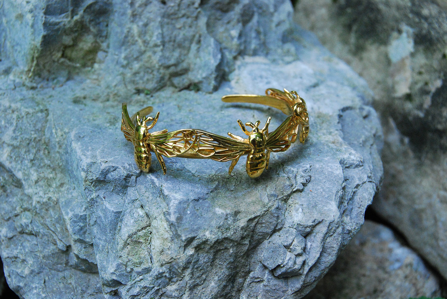Gold bee bracelet cuff placed on stones, from top view,, emphasizing insect-themed design.