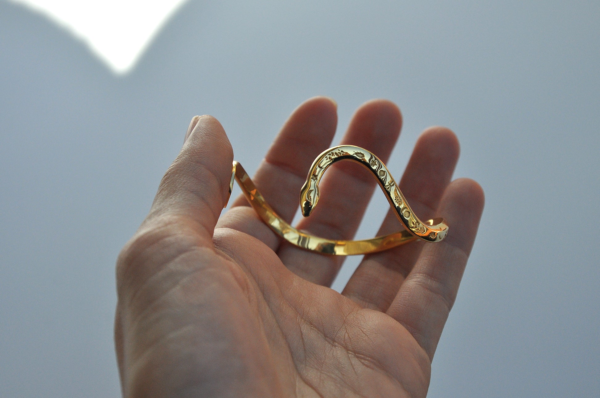 Hand holding a polished gold snake bracelet, showing sculptural curves and engraved celestial details.