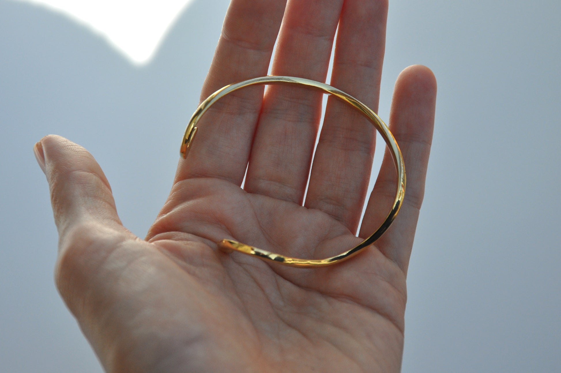 Top view of a hand holding a polished gold snake bracelet, showing its sculptural curves and celestial details.