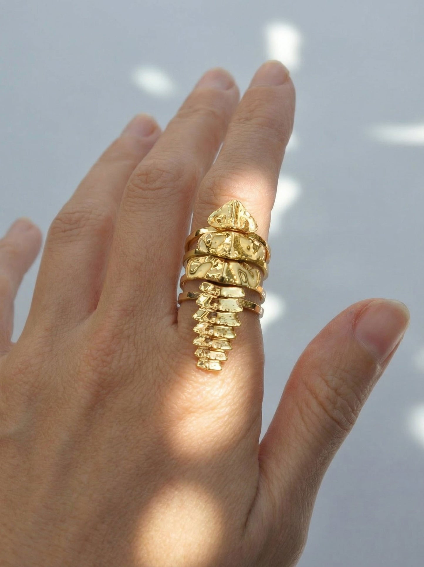 Close‑up of a hand wearing a gold trilobite beetle stacking ring set, with four segmented bands creating a continuous sculptural form.