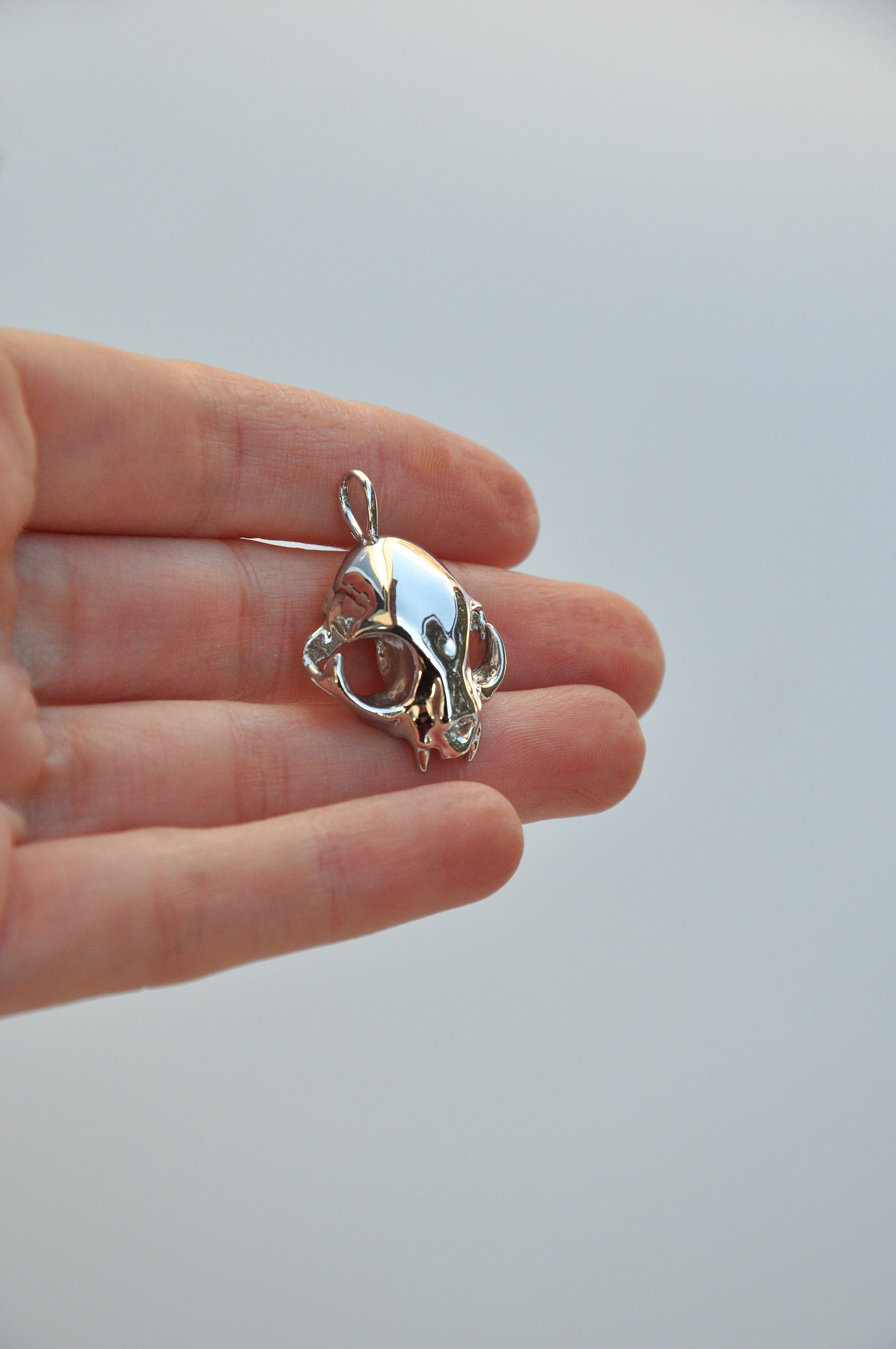 Hand holding the silver feline skull pendant alone, focusing on the intricate design.