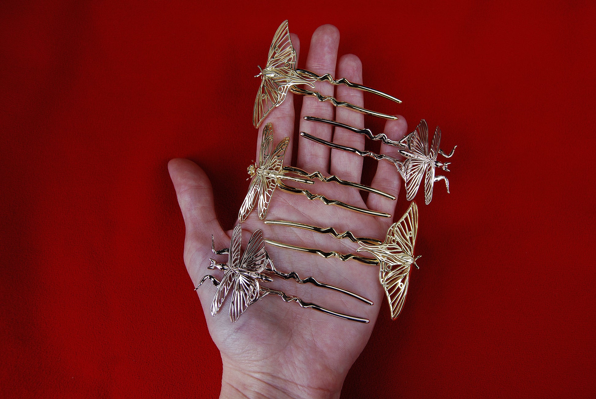 Hand holding three insect-inspired hair pins: one Luna Moth in 14k gold plating, one Luna Moth in solid 14k gold, and one Mantis in 14k rose gold plating, highlighting their intricate craftsmanship and luminous finishes.