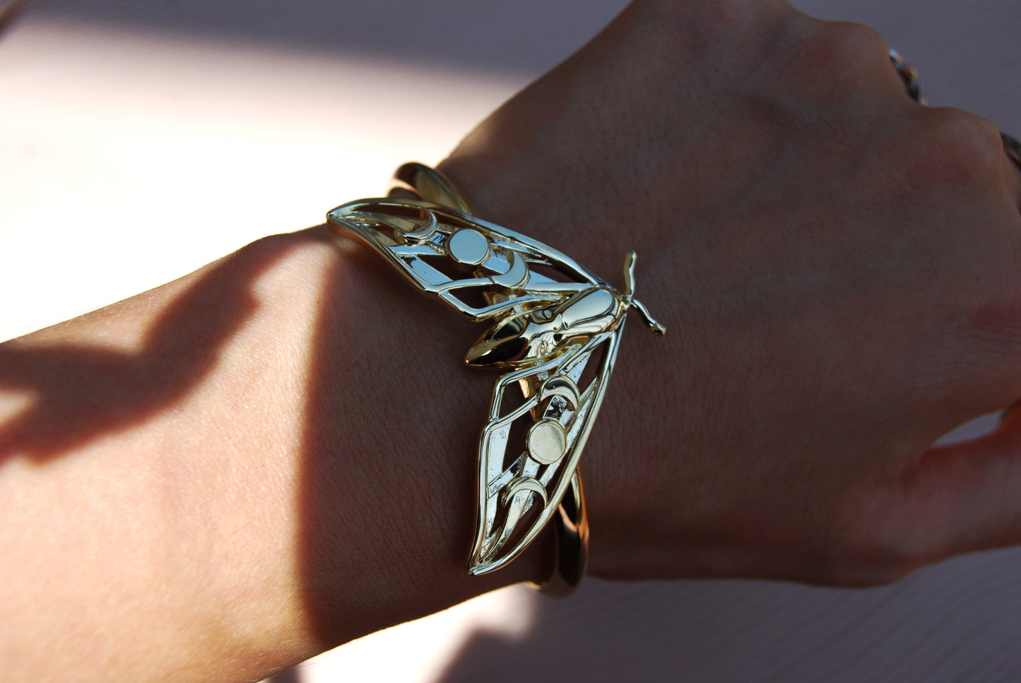 Close-up of Hawk Moth Bracelet in gold, highlighting intricate wing details and celestial moon phase cut-outs.