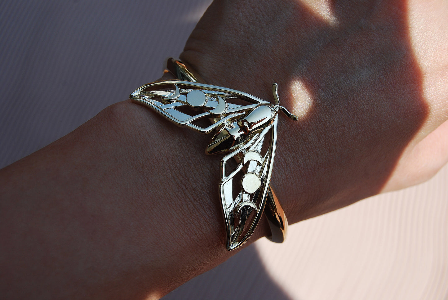 Close-up of Hawk Moth Bracelet in gold on wrist, showing polished finish and delicate moon phase cut-out details.