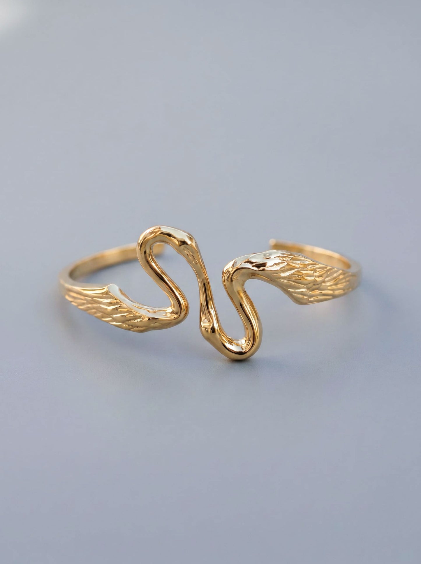 Heron Kiss Bracelet Cuff in gold finish, photographed in sunlight, showing sculptural winged ends curving toward each other in mirrored symmetry.