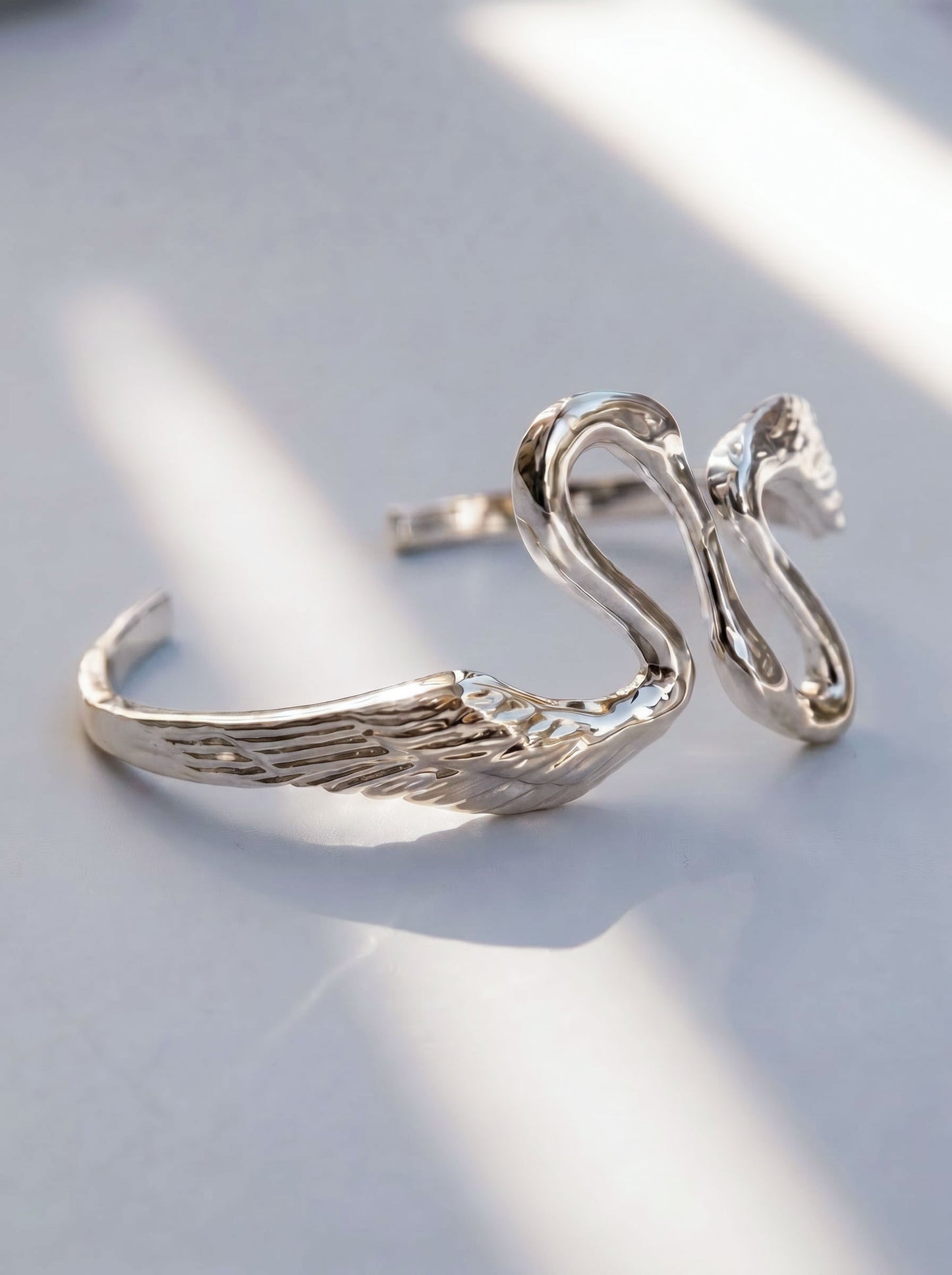 Heron Kiss Bracelet Cuff in silver finish, photographed flat under natural light, showing mirrored wing forms and crisp sculptural detail.