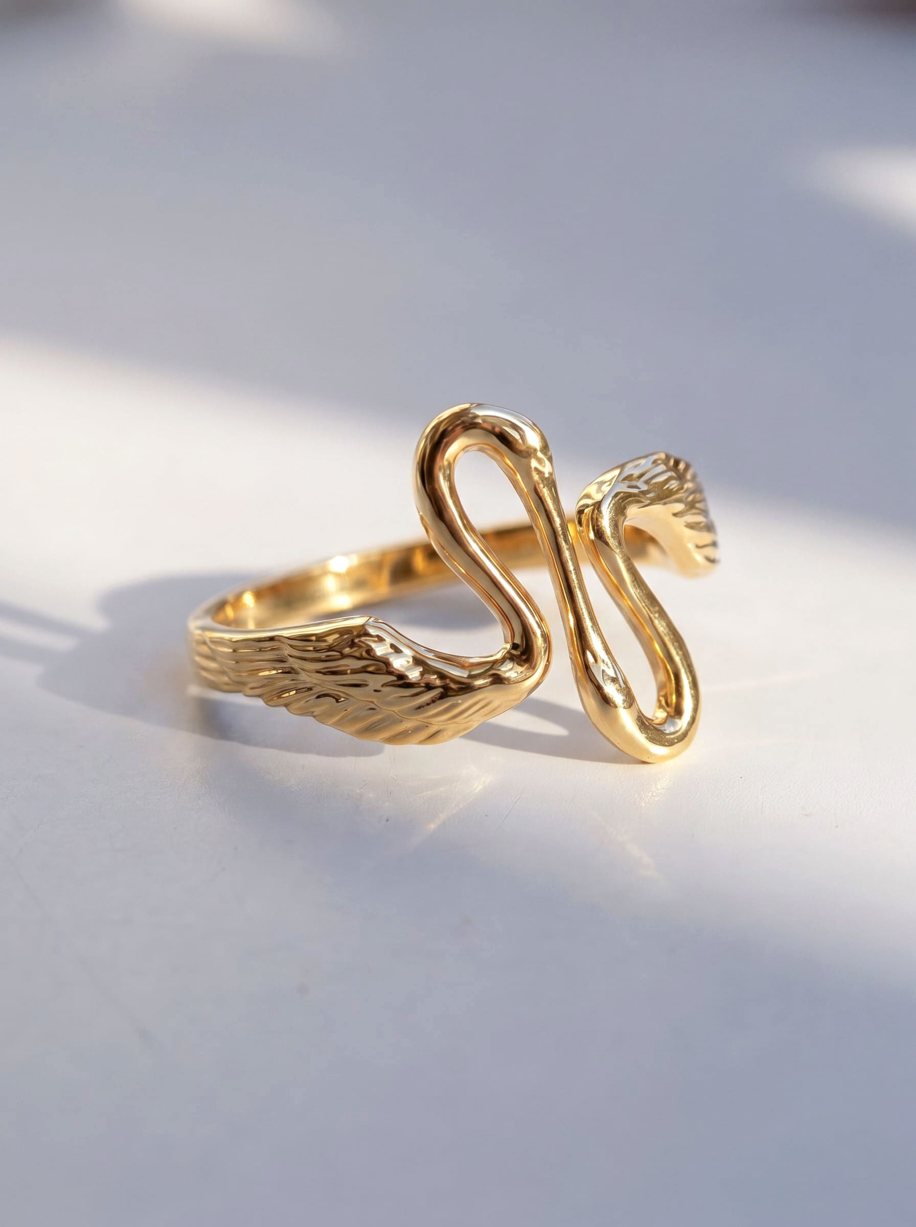 Heron Kiss Ring in gold finish, photographed in sunlight, showing two sculpted herons meeting in mirrored symmetry.