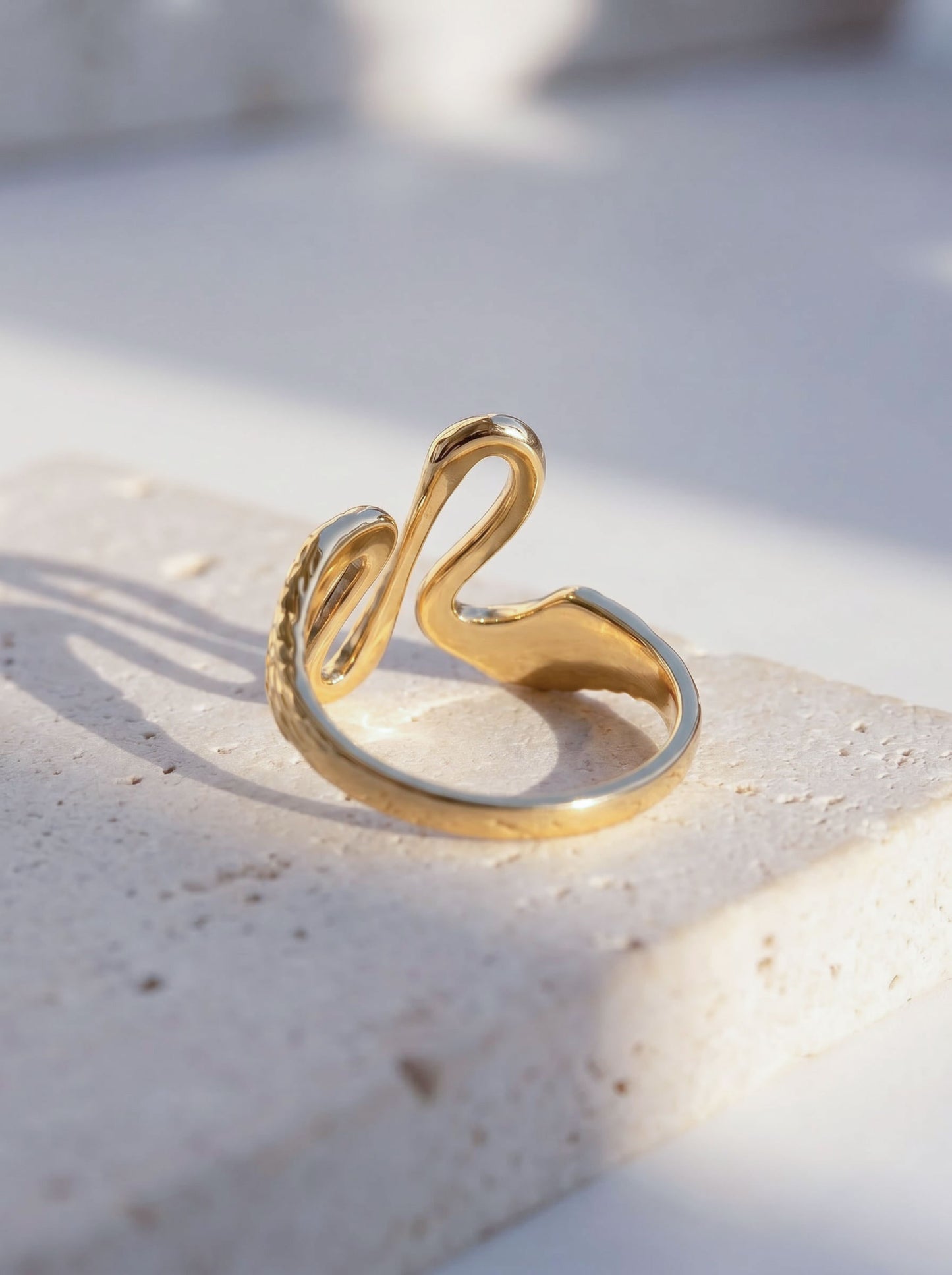 Heron Kiss Ring resting on stone surface, emphasizing polished gold texture and engraved feather detail.