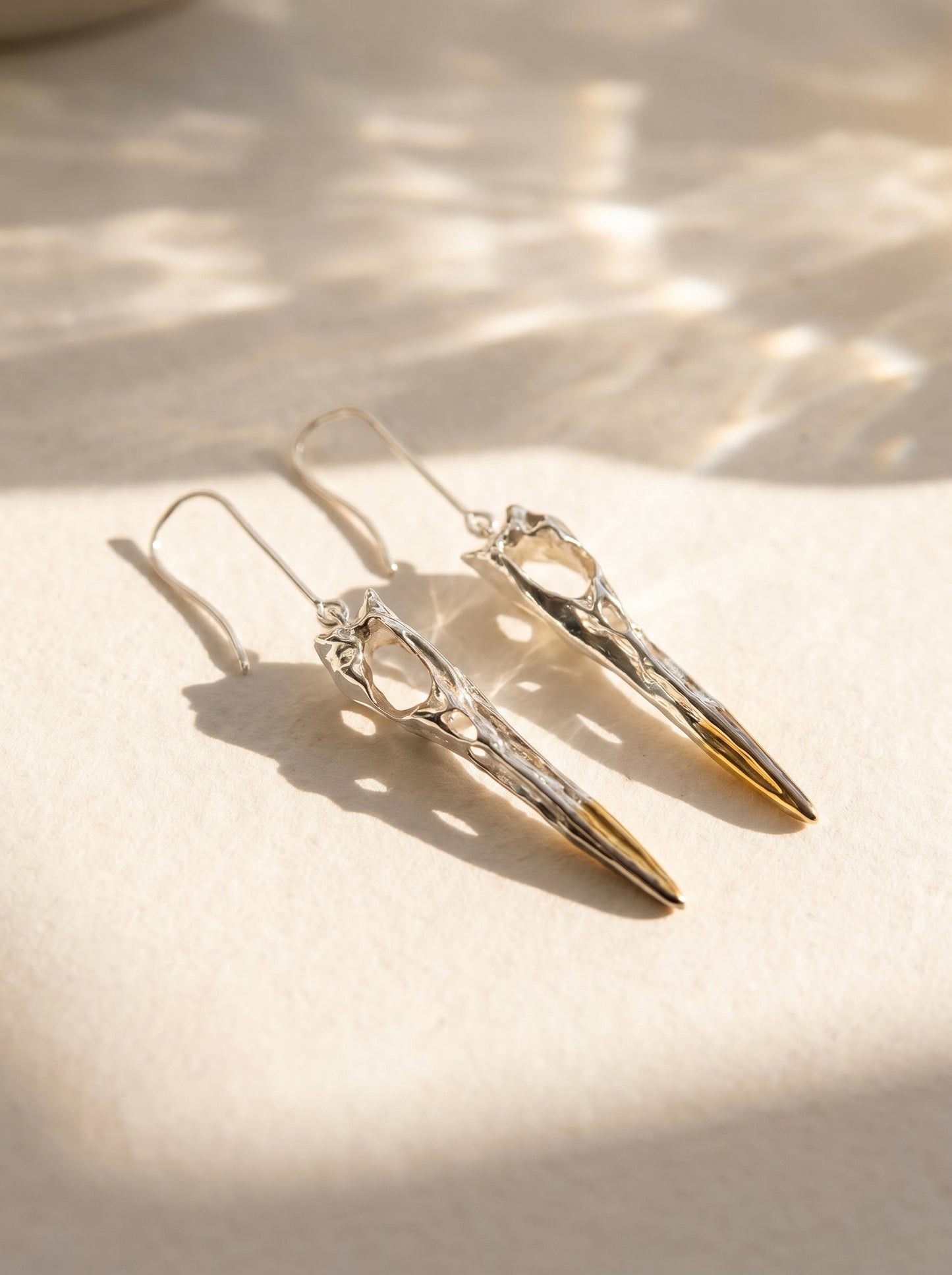 Pair of Heron Skull Earrings photographed flat, showing gold‑plated rear tips and black rhodium front accents.