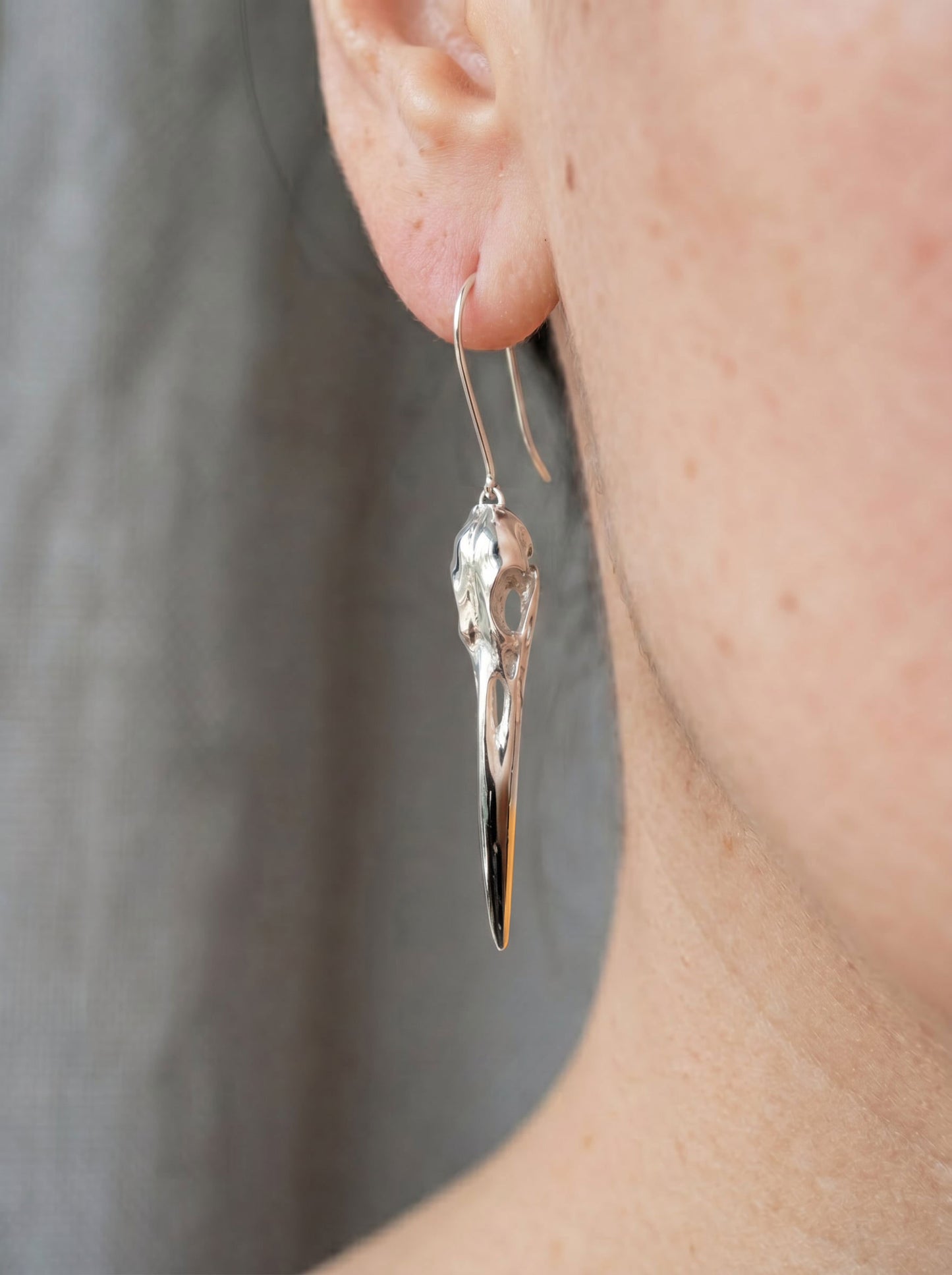 Heron Skull Earrings worn on ear, showing slender drop silhouette and mixed‑metal finish that elongates the neck.