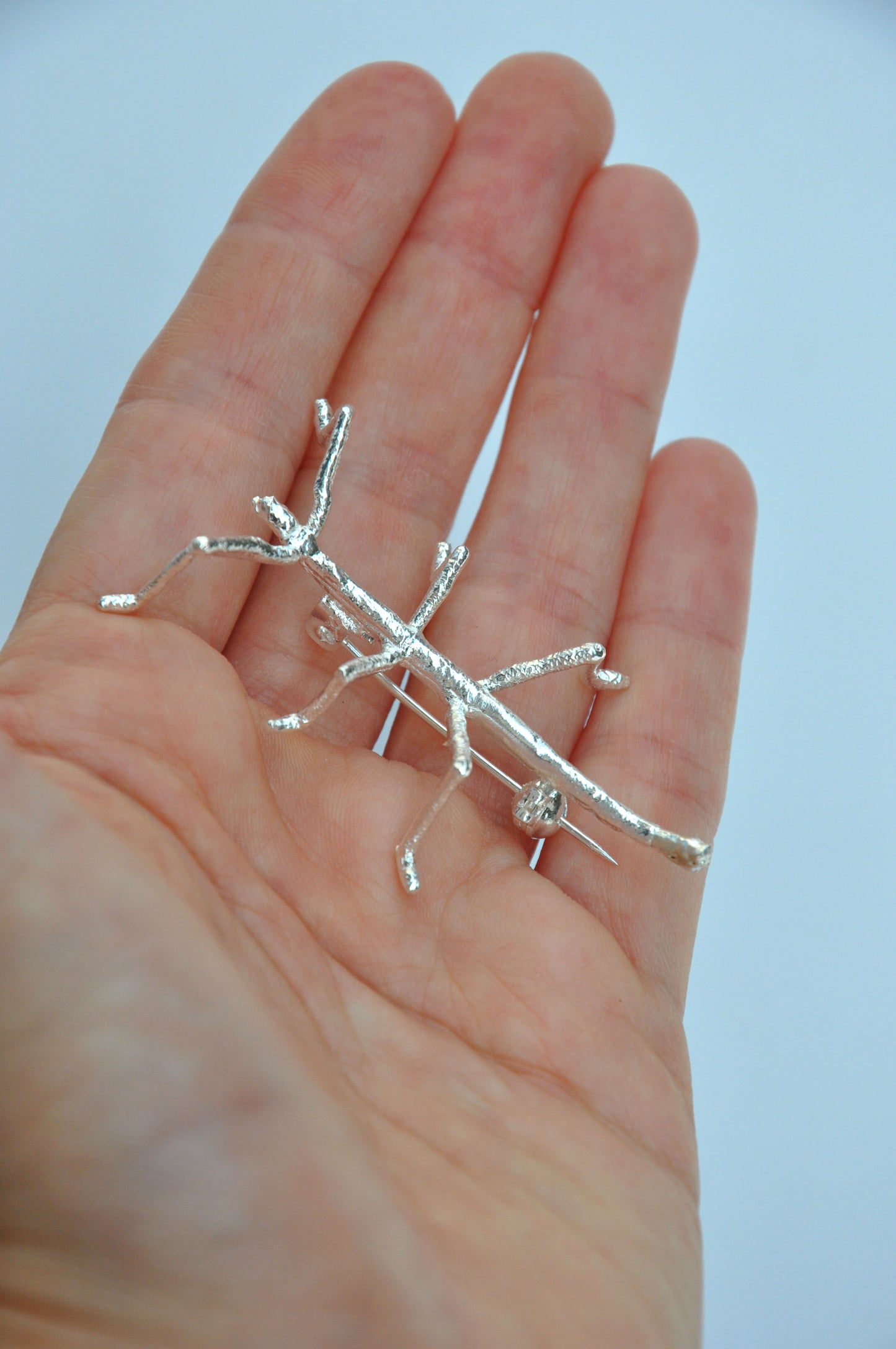 side view of the silver insect brooch resting on a hand, styled as a wearable nature-inspired accessory.