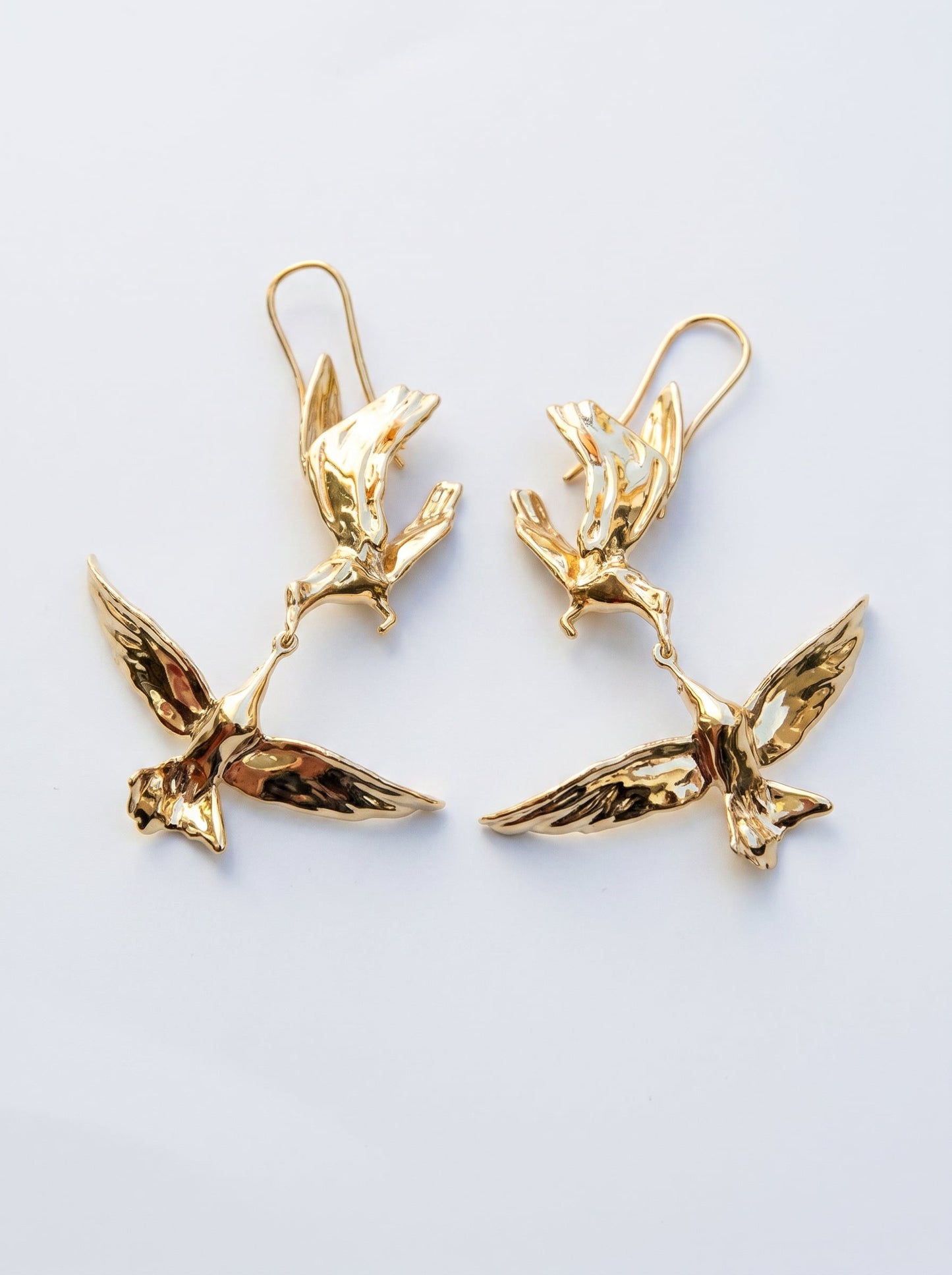 Kiss in Flight Arctic Tern Earrings in gold finish, photographed in sunlight, showing two sculpted birds meeting mid‑air in mirrored symmetry.