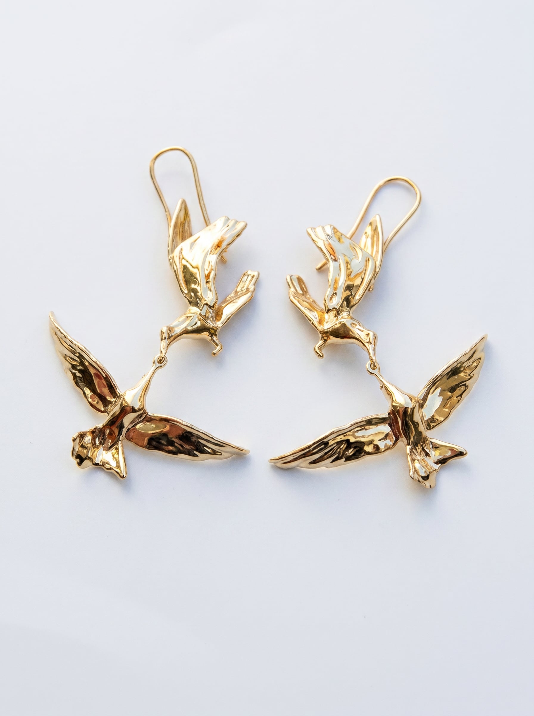 Kiss in Flight Arctic Tern Earrings in gold finish, photographed in sunlight, showing two sculpted birds meeting mid‑air in mirrored symmetry.