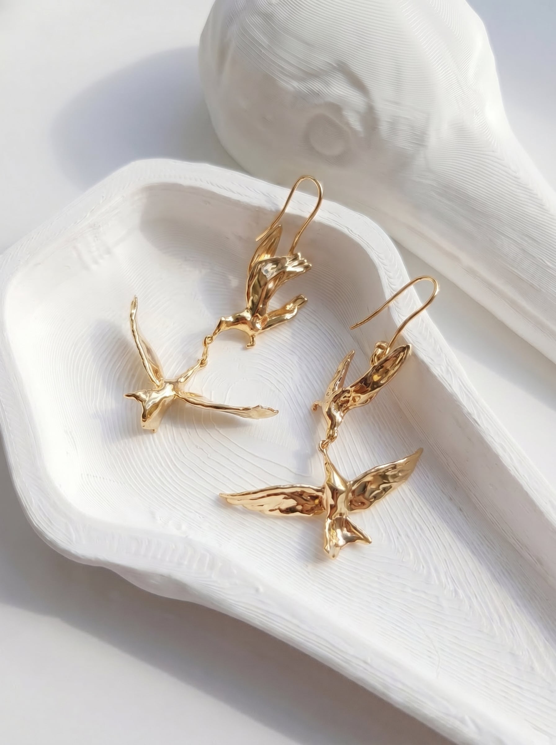 Kiss in Flight Arctic Tern Earrings displayed on white tray, showing polished gold texture and delicate wing engraving.