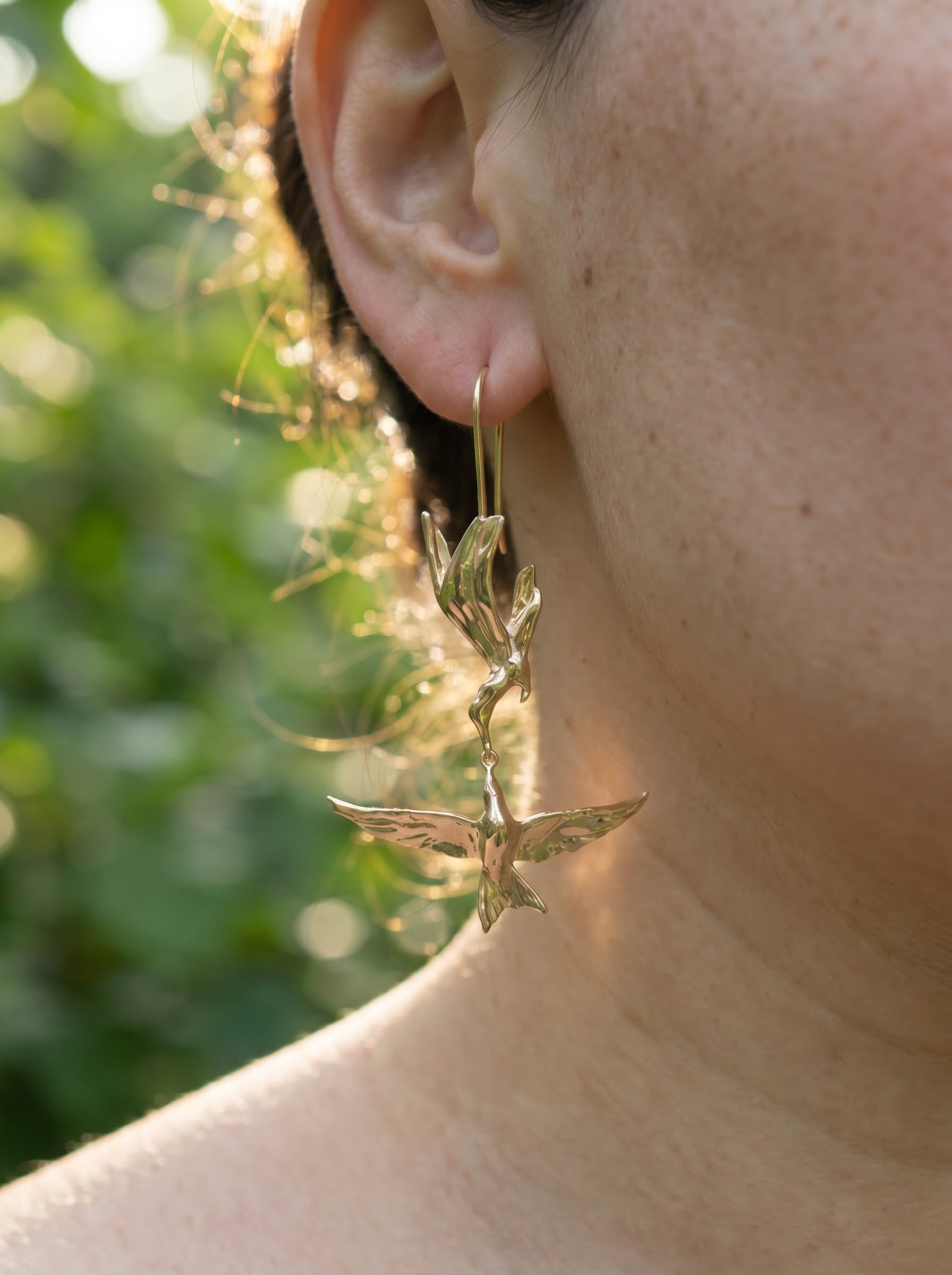 Close‑up of Kiss in Flight Arctic Tern Earrings worn on ear, highlighting the tender mirrored bird design and soft golden glow.