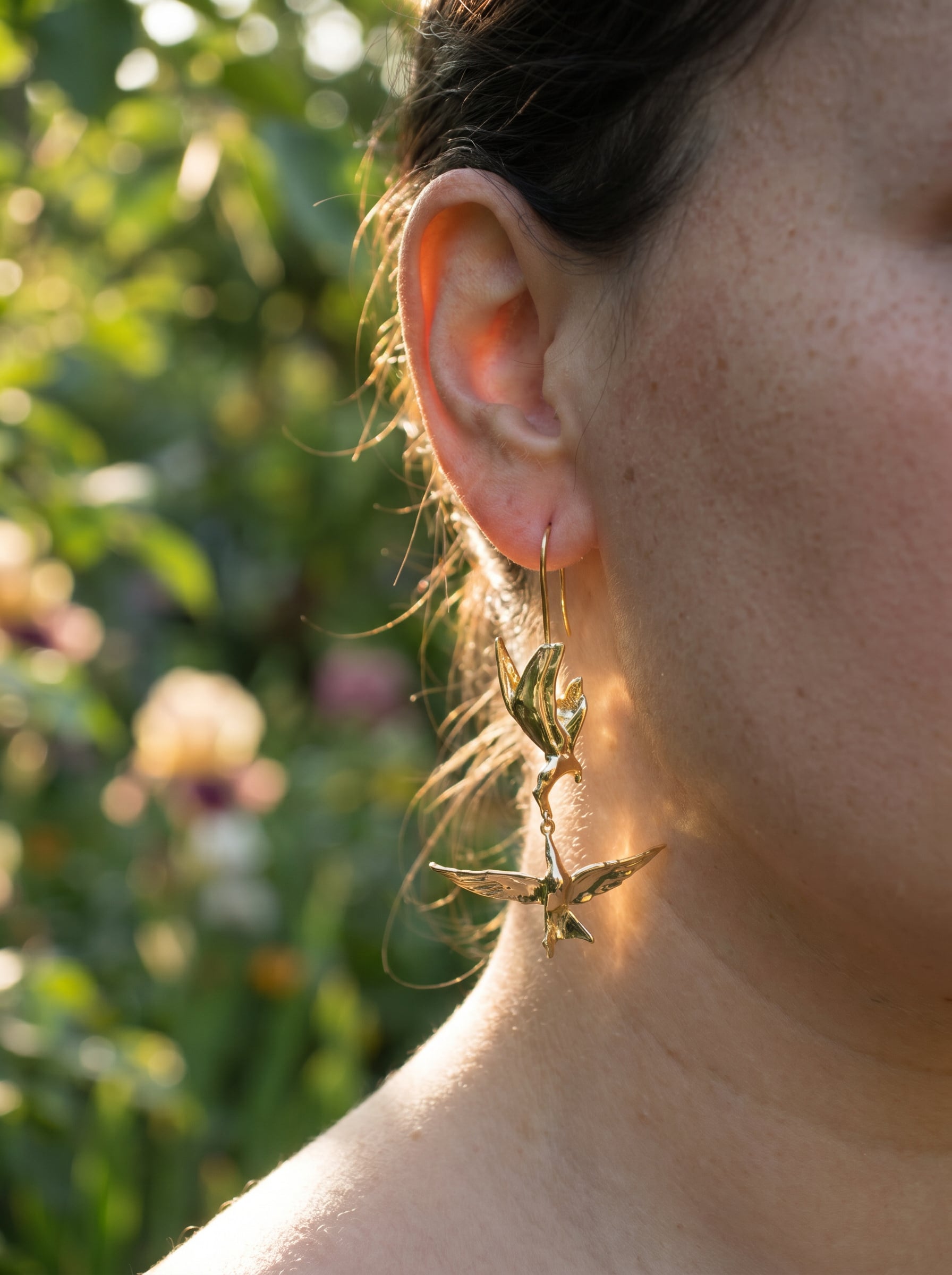 Kiss in Flight Arctic Tern Earrings worn outdoors, showing mirrored birds and luminous gold finish against natural light.