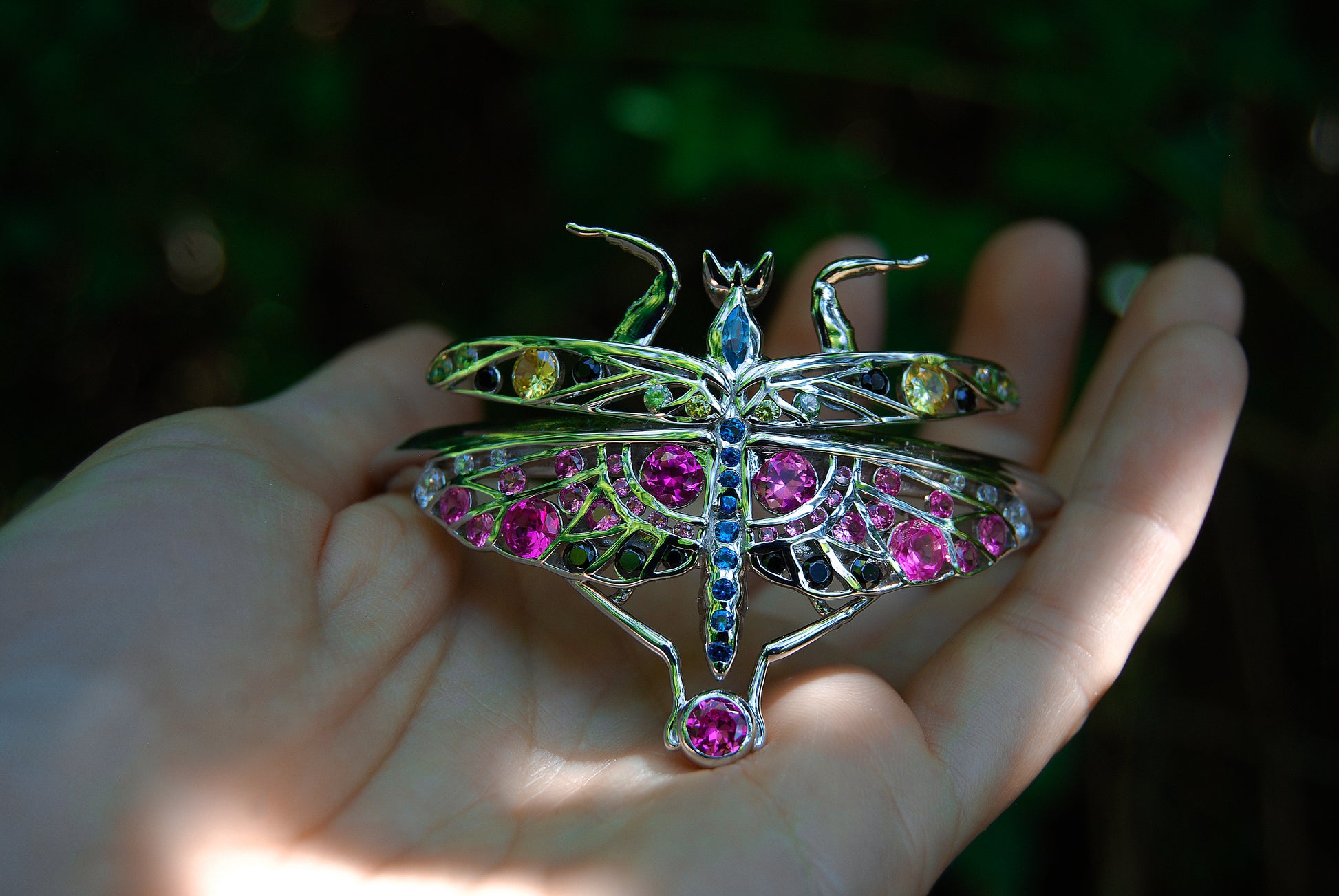 Close-up of sterling silver mantis bracelet with enamel and zirconia stones worn on hand in natural outdoor setting