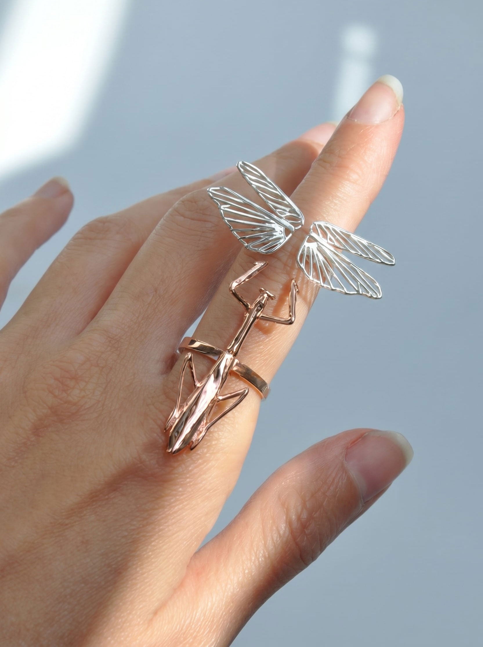 Praying mantis ring with sterling‑silver wings and a rose‑gold body shown on the hand.