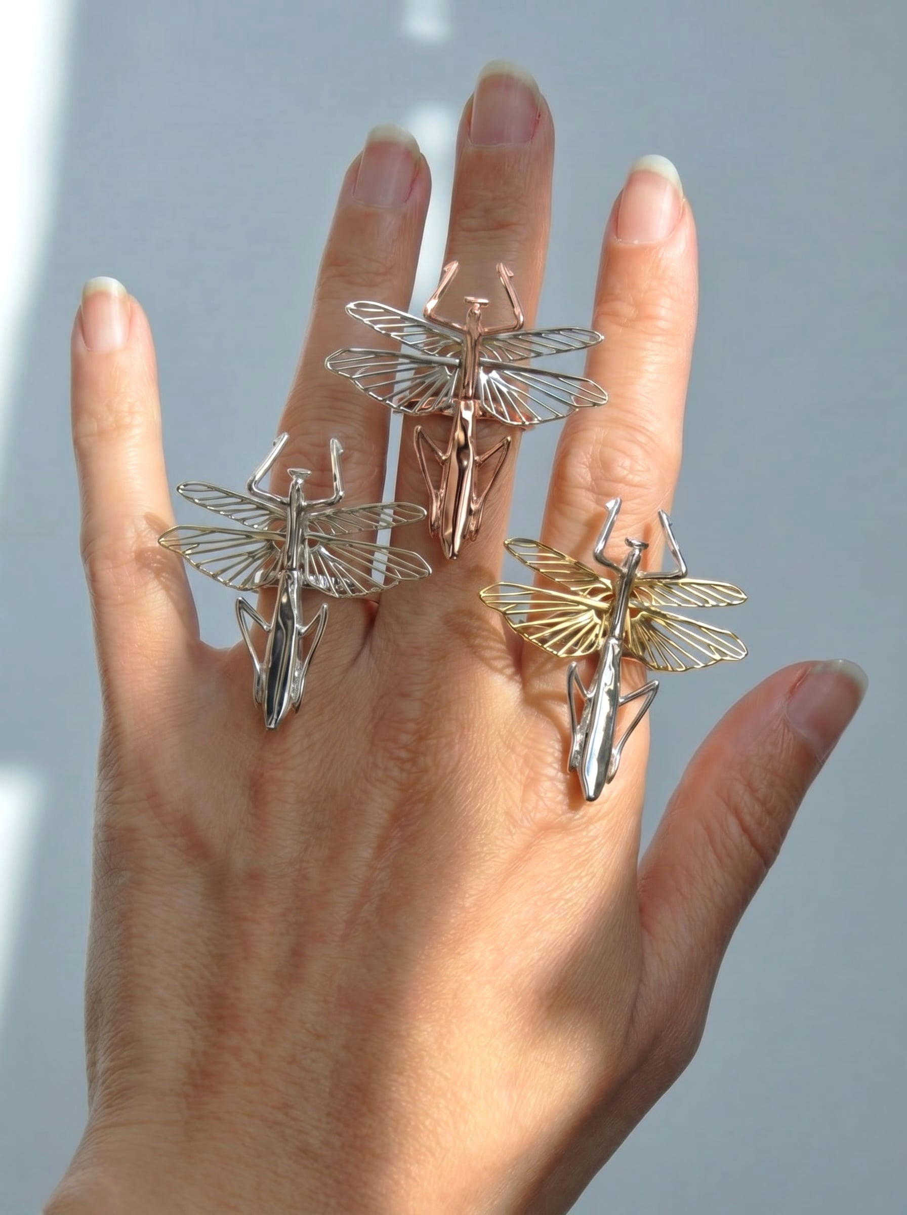 Three praying mantis rings shown on the hand in sterling silver, 14k gold‑plated, and rose‑gold plated finishes.