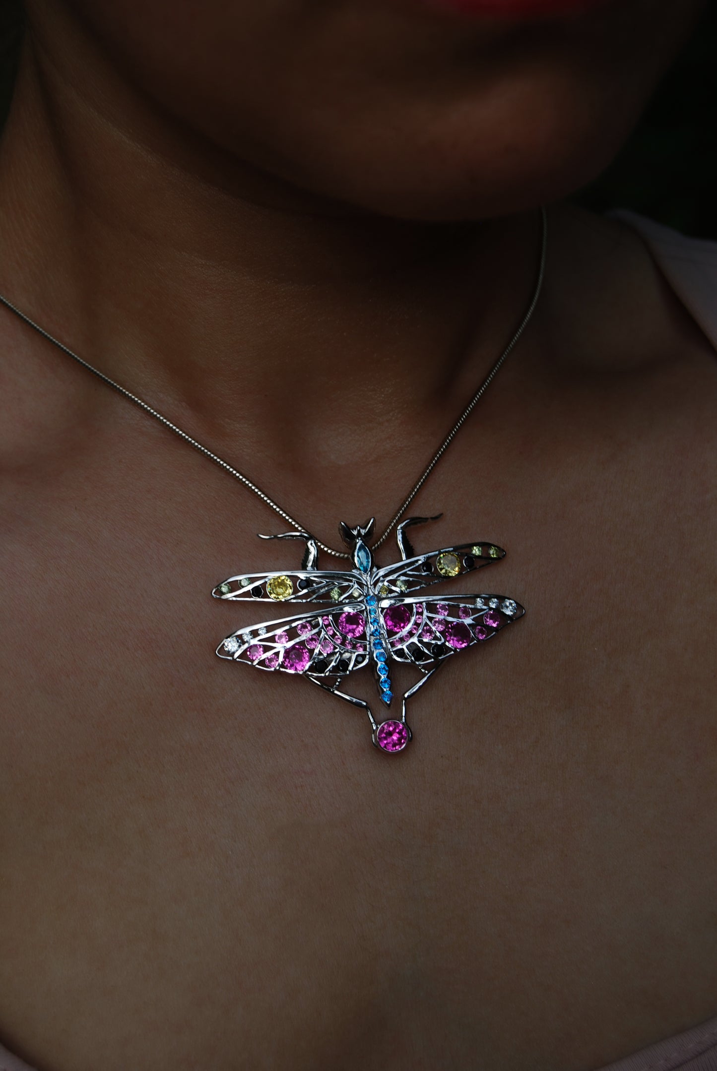 Model wearing silver praying mantis pendant and bracelet, styled against white background to highlight elegant insect-inspired jewelry design