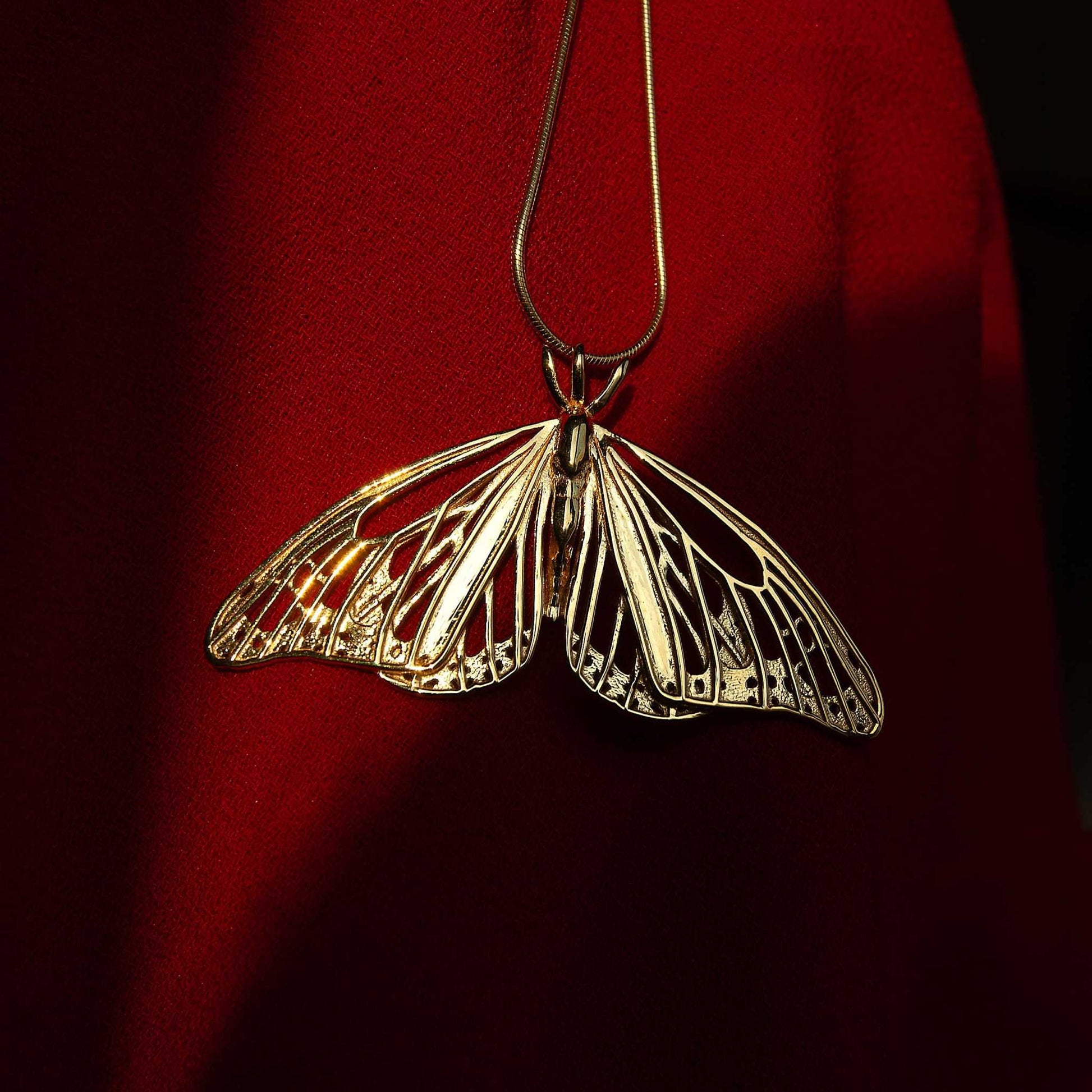 Close-up of gold Monarch Butterfly pendant on red background, showing fine sculptural details.