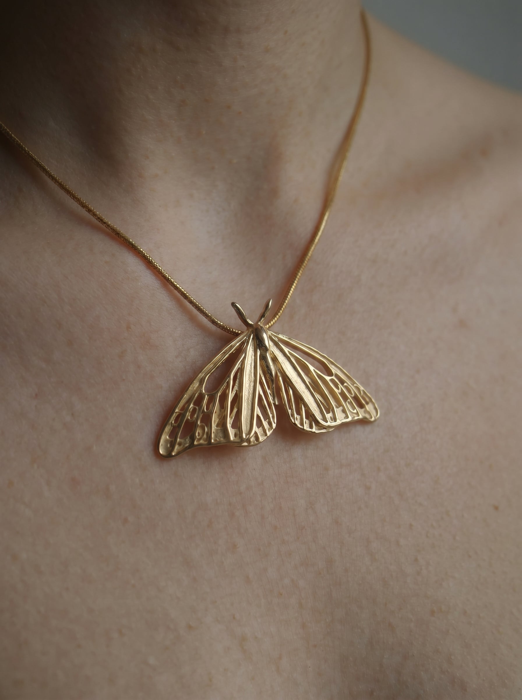 Minimal view of gold Monarch Butterfly pendant worn on the neck, highlighting its airy silhouette.
