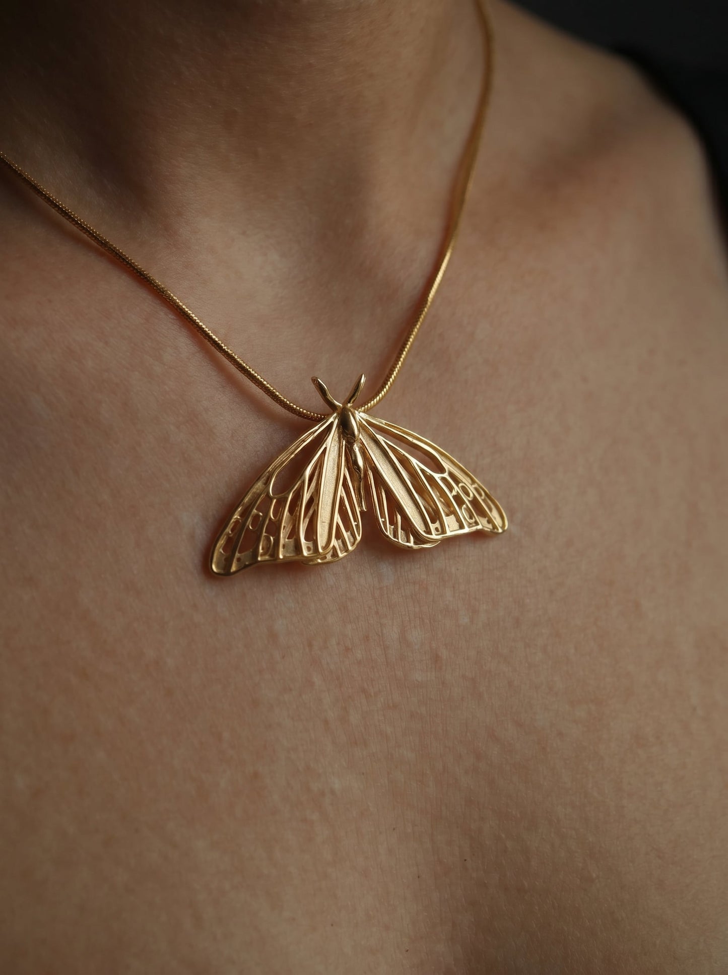 Gold Monarch Butterfly pendant worn on a thin chain, shown against bare skin.