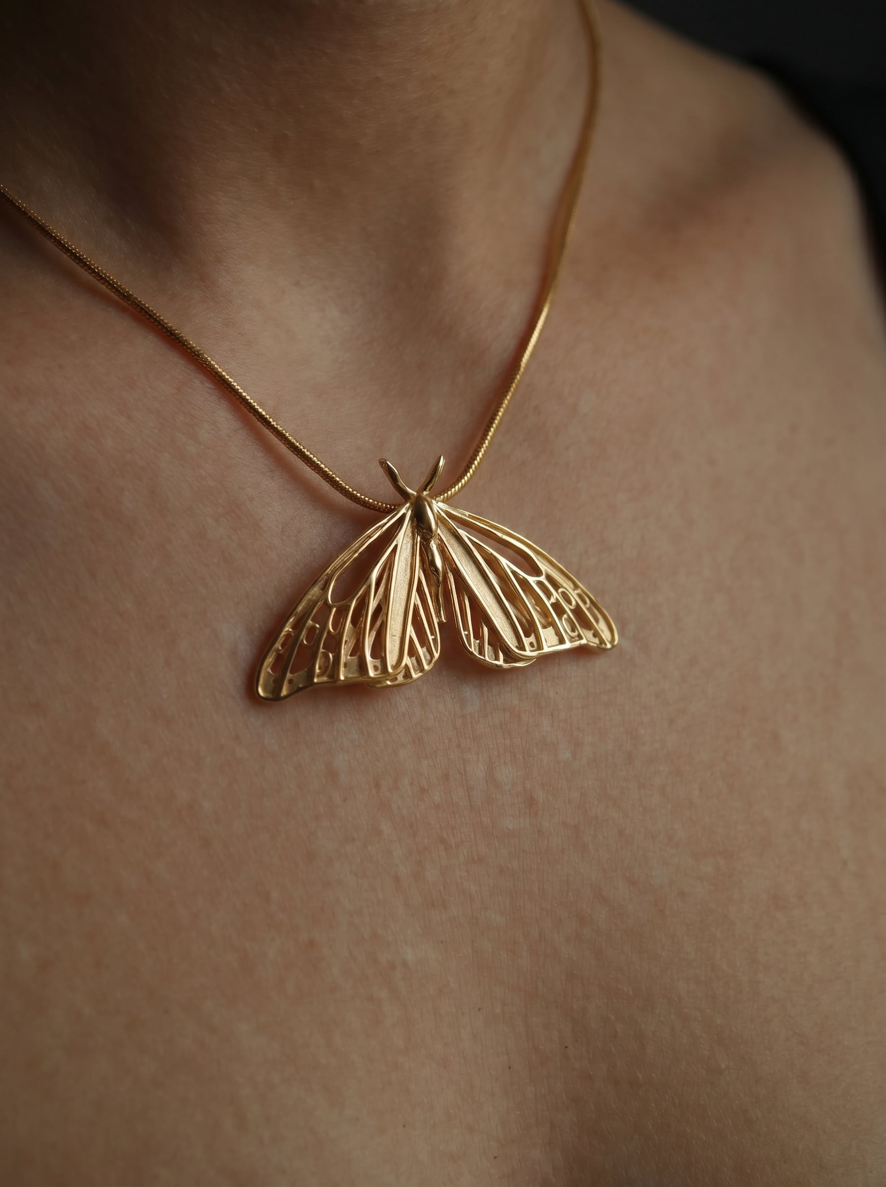 Gold Monarch Butterfly pendant worn on a thin chain, shown against bare skin.
