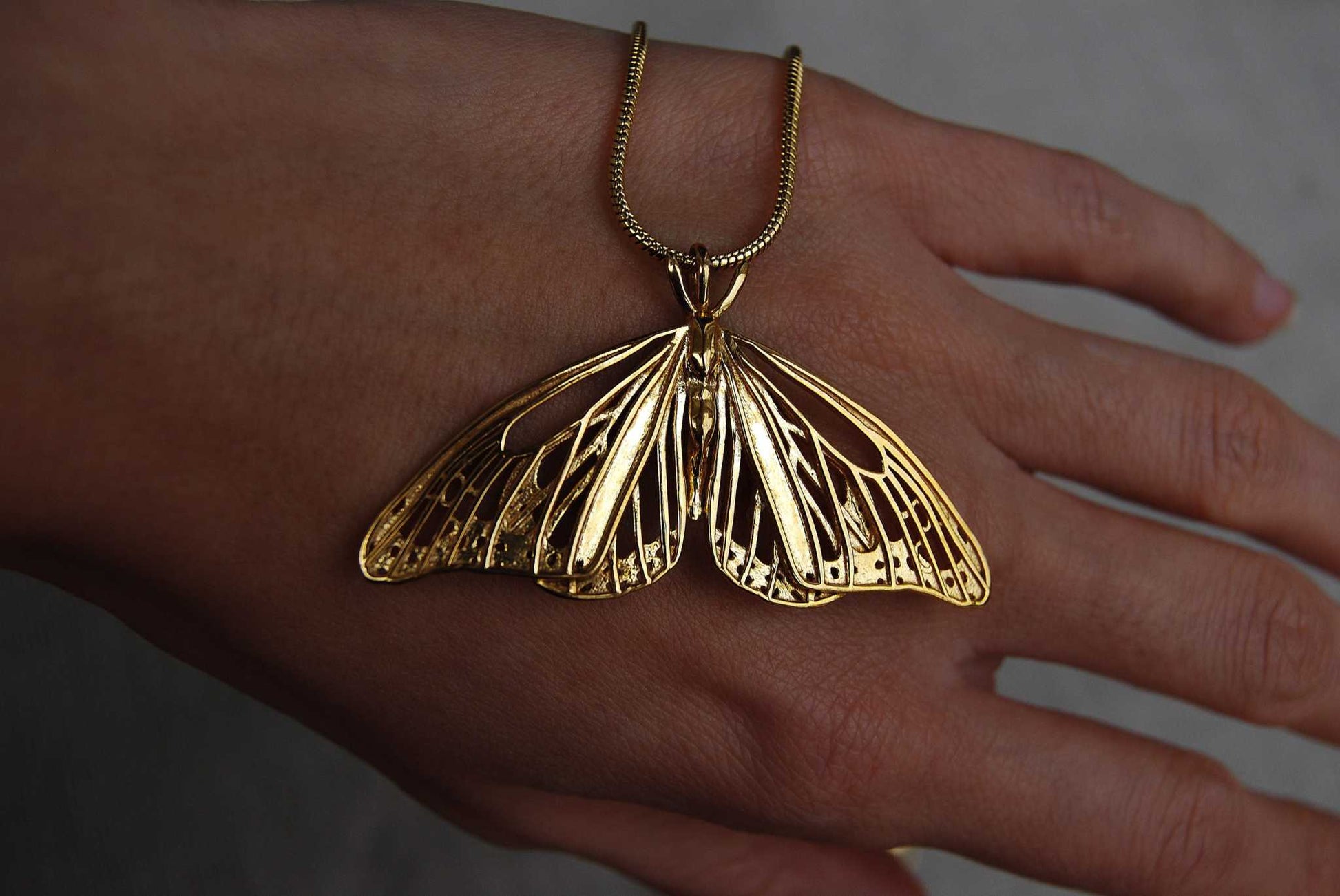 Gold Monarch Butterfly pendant held in hand, showing scale and polished surface.