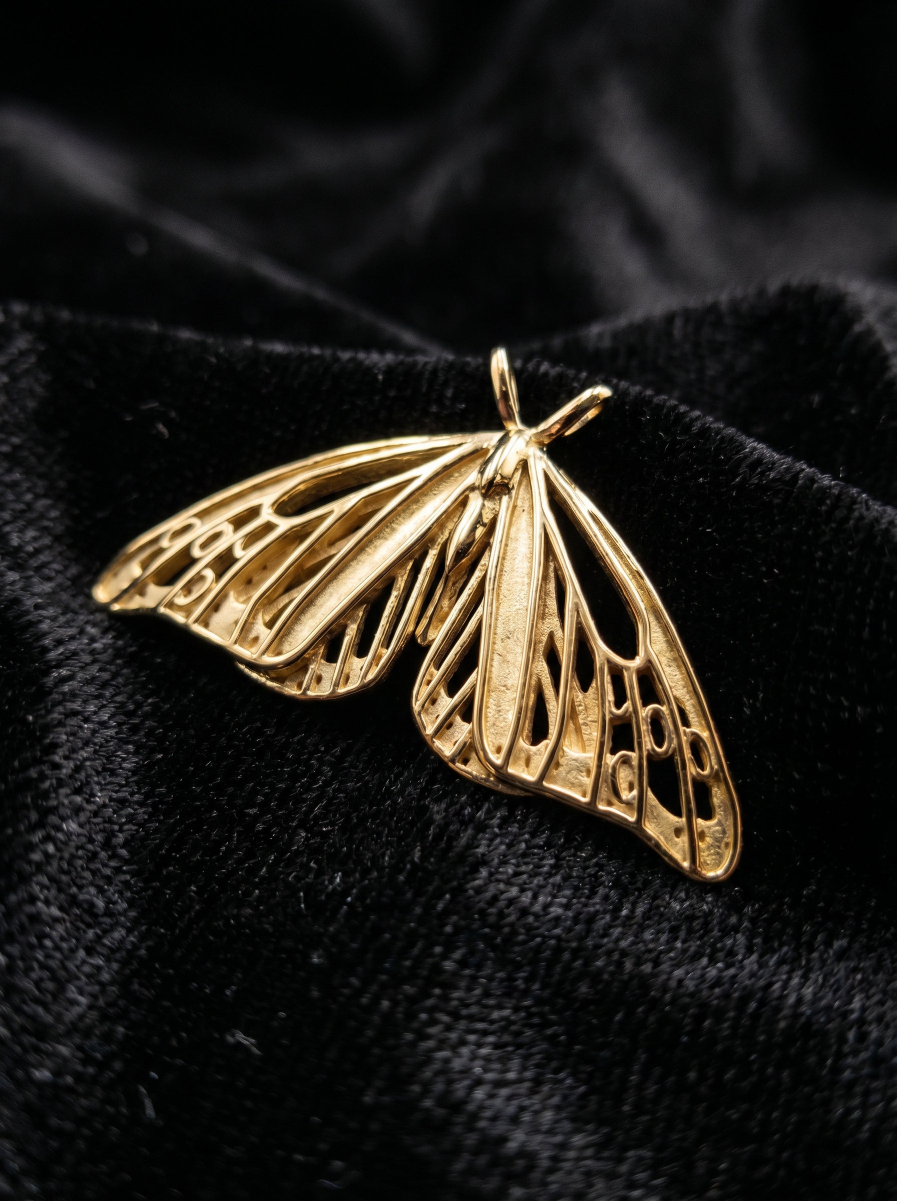 Gold Monarch Butterfly pendant photographed on black satin, showing detailed wing cutouts.