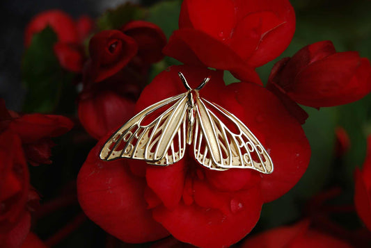 14k gold Monarch Butterfly pendant resting on red petals, highlighting its sculptural openwork wings.