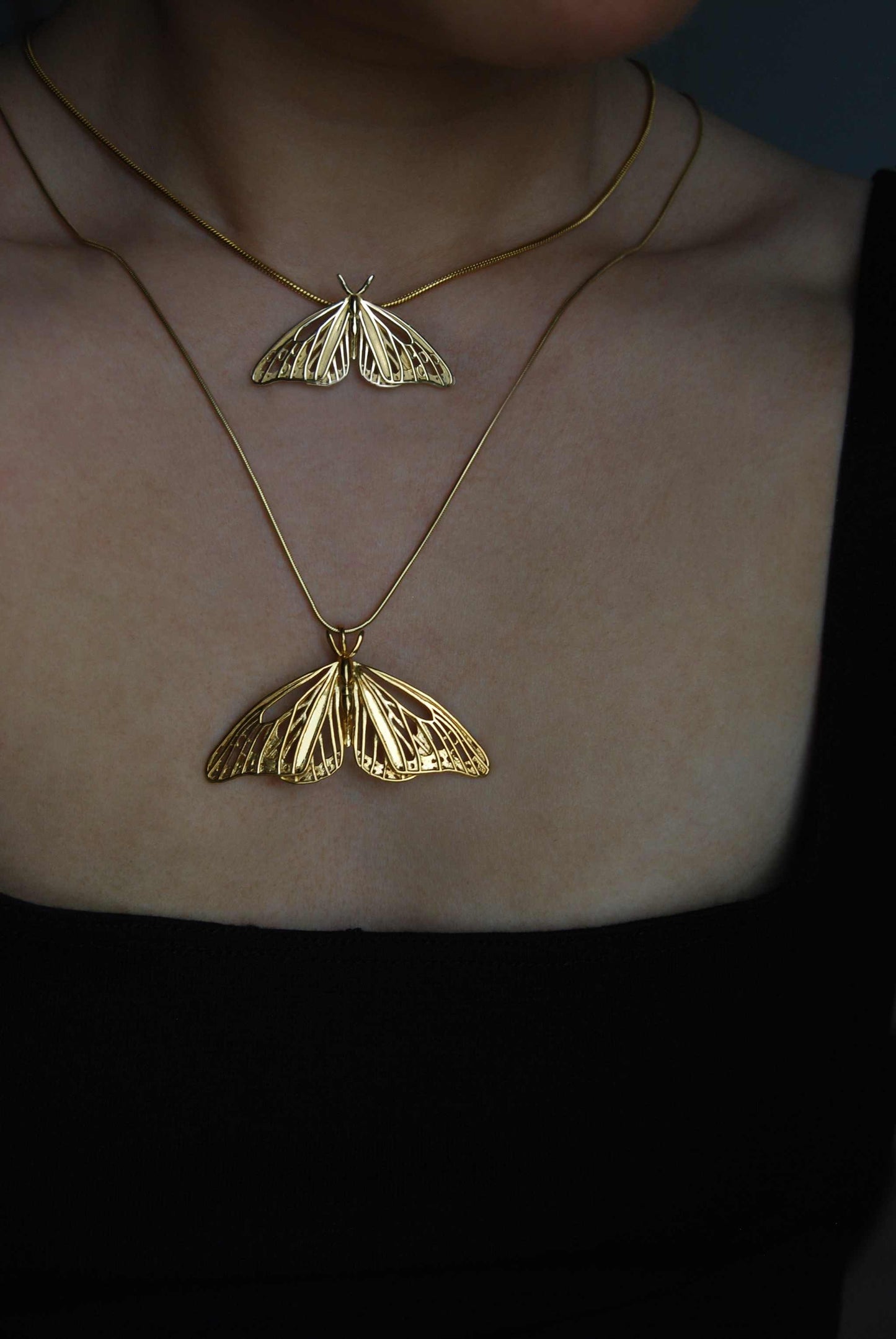 Two gold Monarch Butterfly pendants in small and large sizes worn layered on the neck, showing sculptural openwork wings and polished finish.