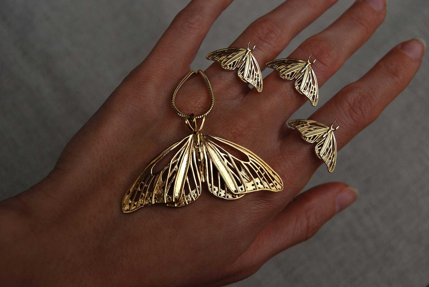 Gold Monarch Butterfly pendant paired with matching sculptural rings, photographed on hand.