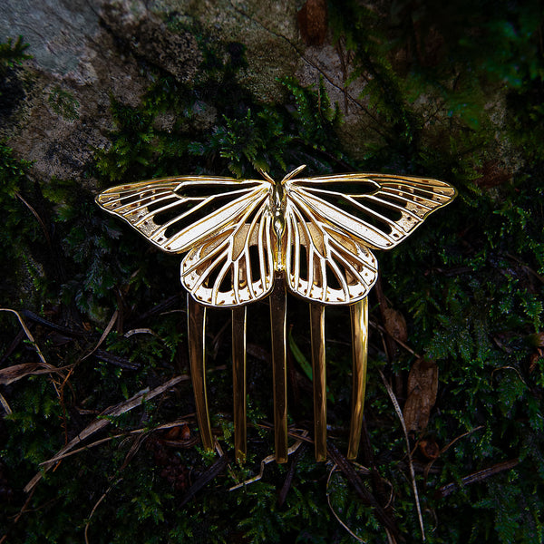 Front view of a 14k gold plated Monarch Butterfly hair comb set against a lush forest backdrop. The comb’s radiant wings gleam in natural light, echoing the elegance of woodland creatures and blending seamlessly with the organic textures of moss, bark, and leaves.