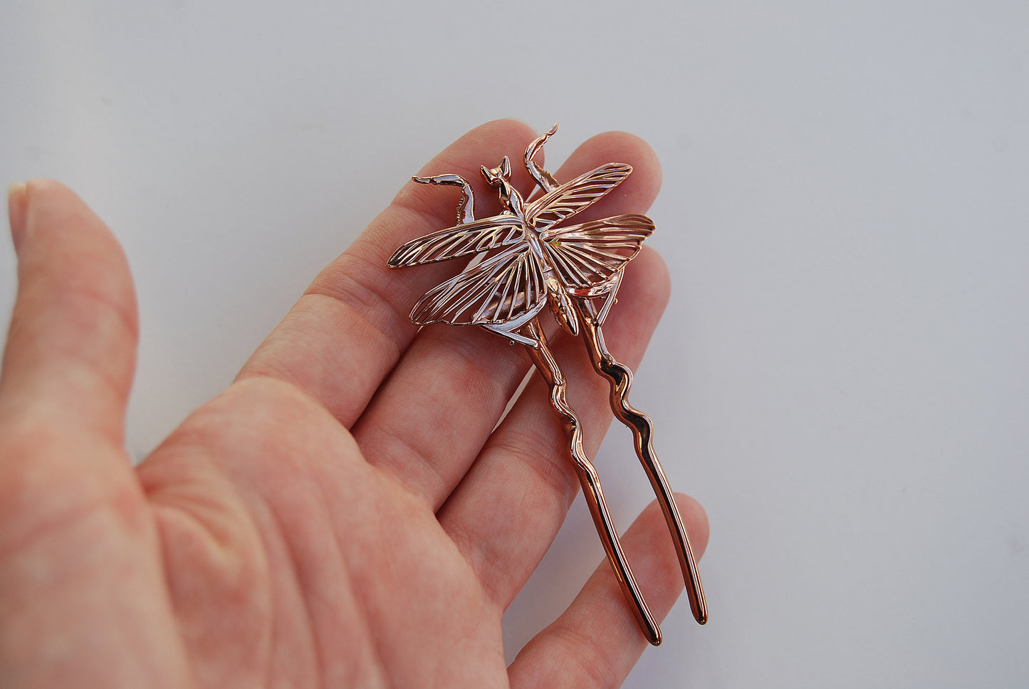 Detailed view of Orchid Mantis hairpins resting on palm, metallic and surreal.