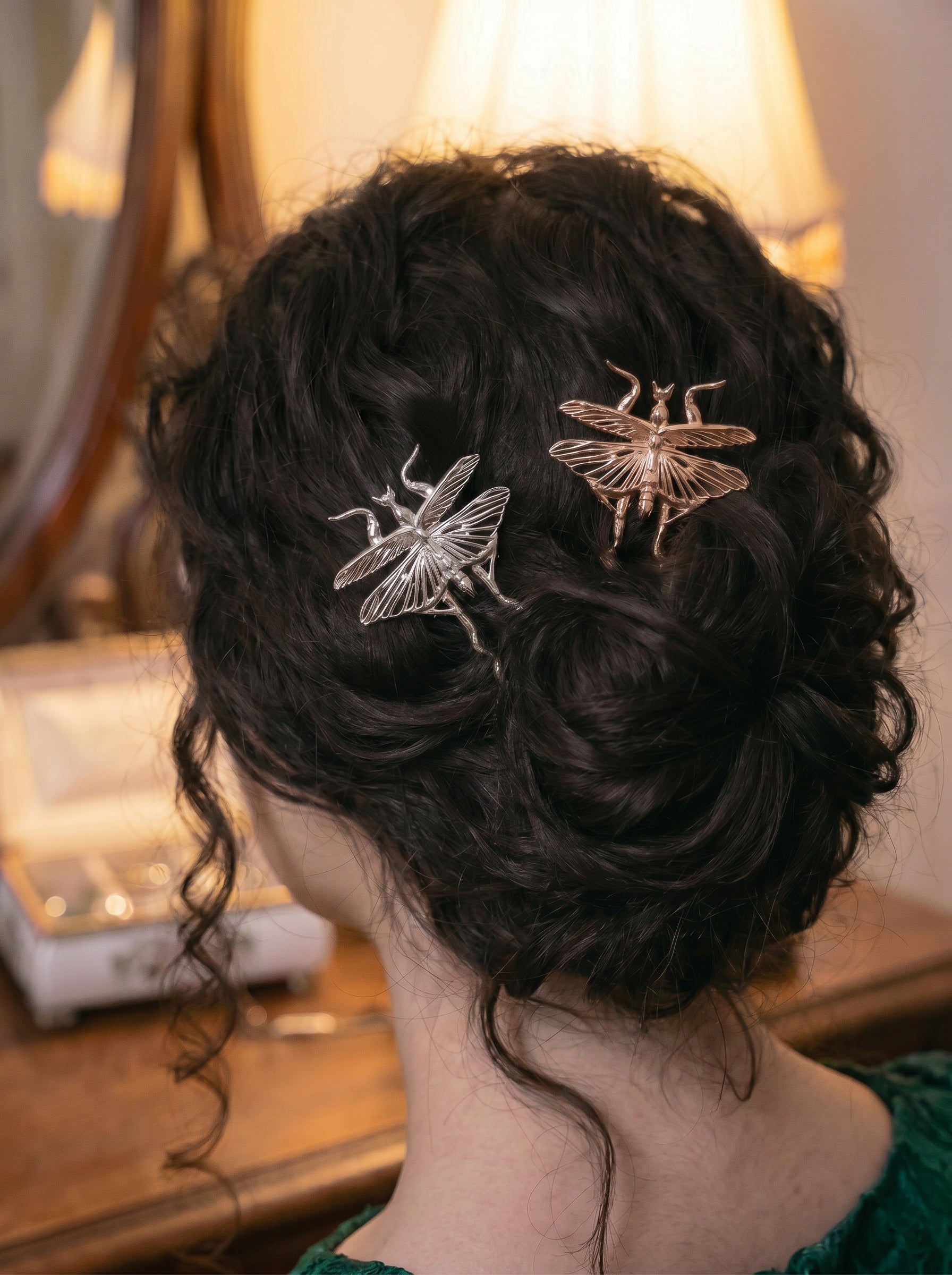Silver and rose gold Orchid Mantis hairpins styled in dark curls under warm vintage lamplight.