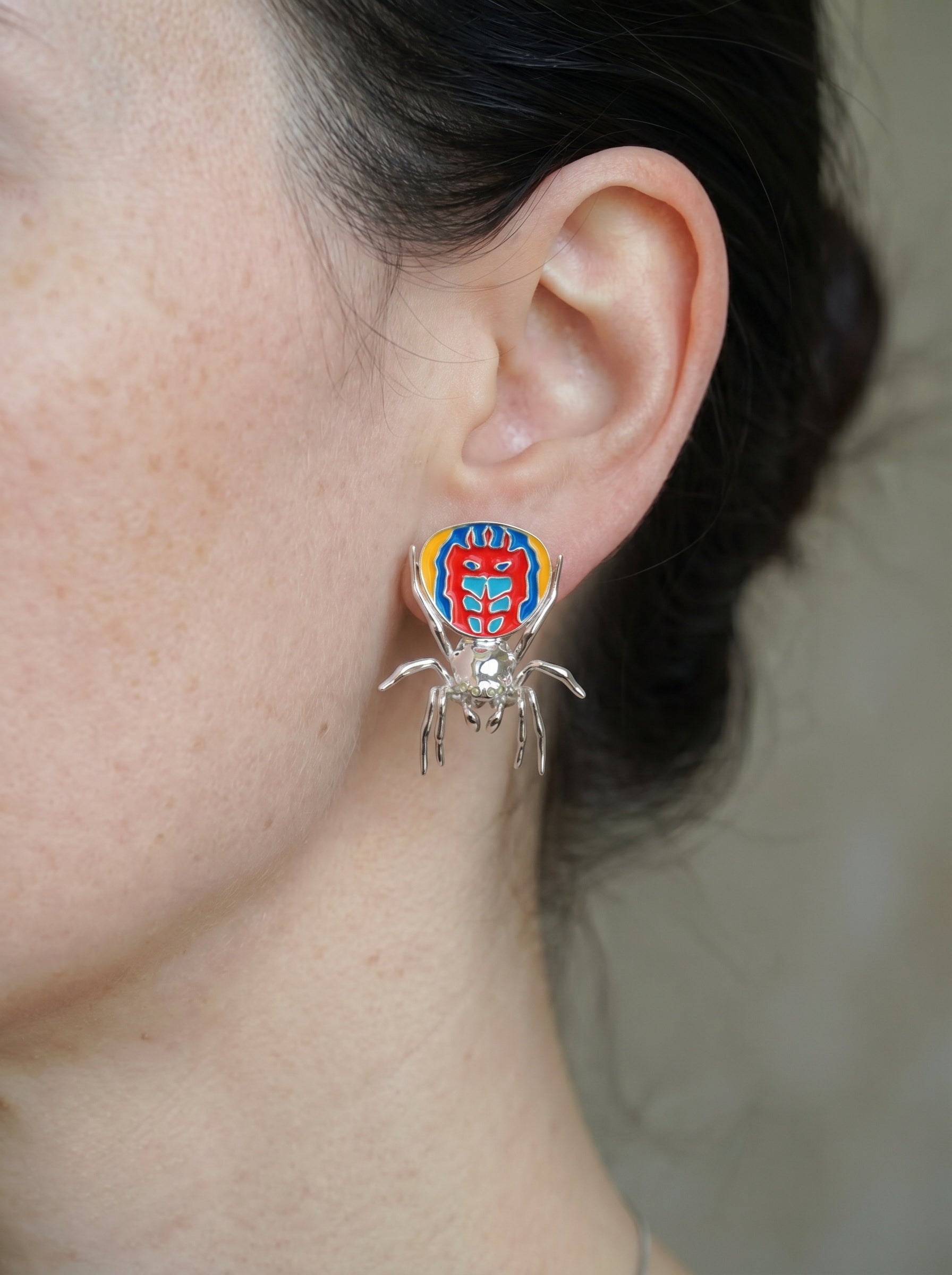 Sterling‑silver peacock spider earring with vibrant enamel detailing worn on the ear.