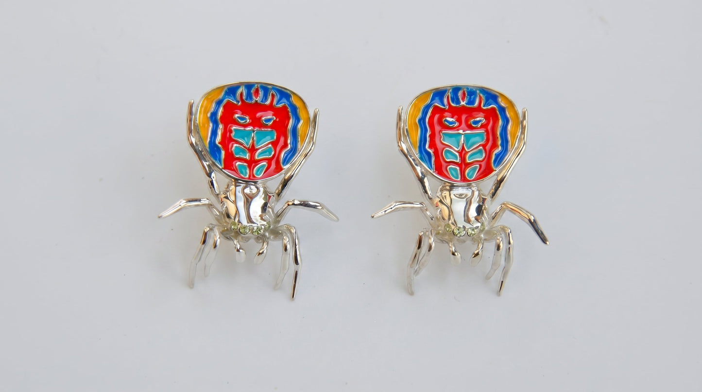 Pair of peacock spider earrings with vibrant enamel detailing displayed on a white background.
