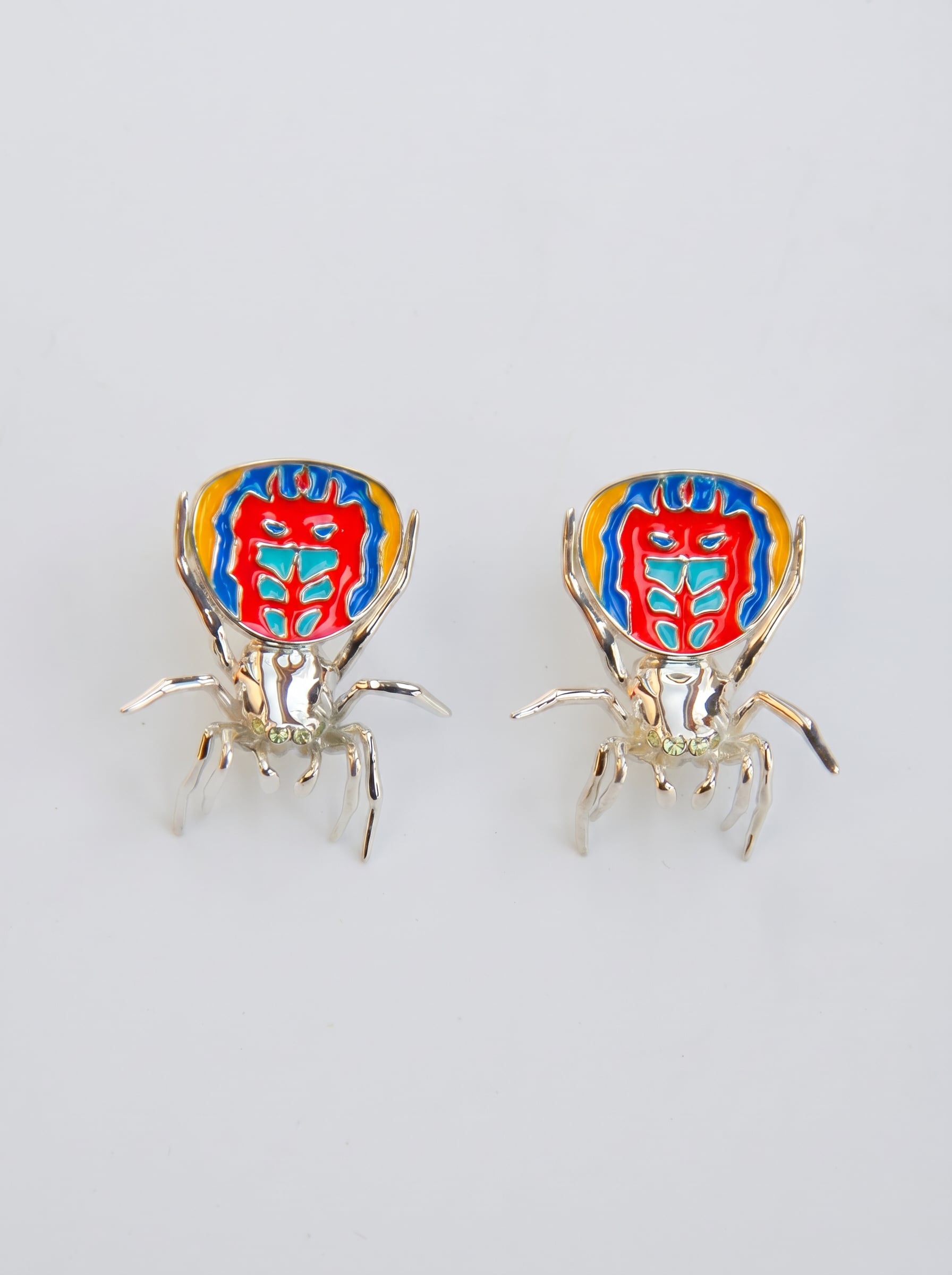 Pair of sterling‑silver peacock spider earrings with vibrant enamel detailing displayed on a white background.