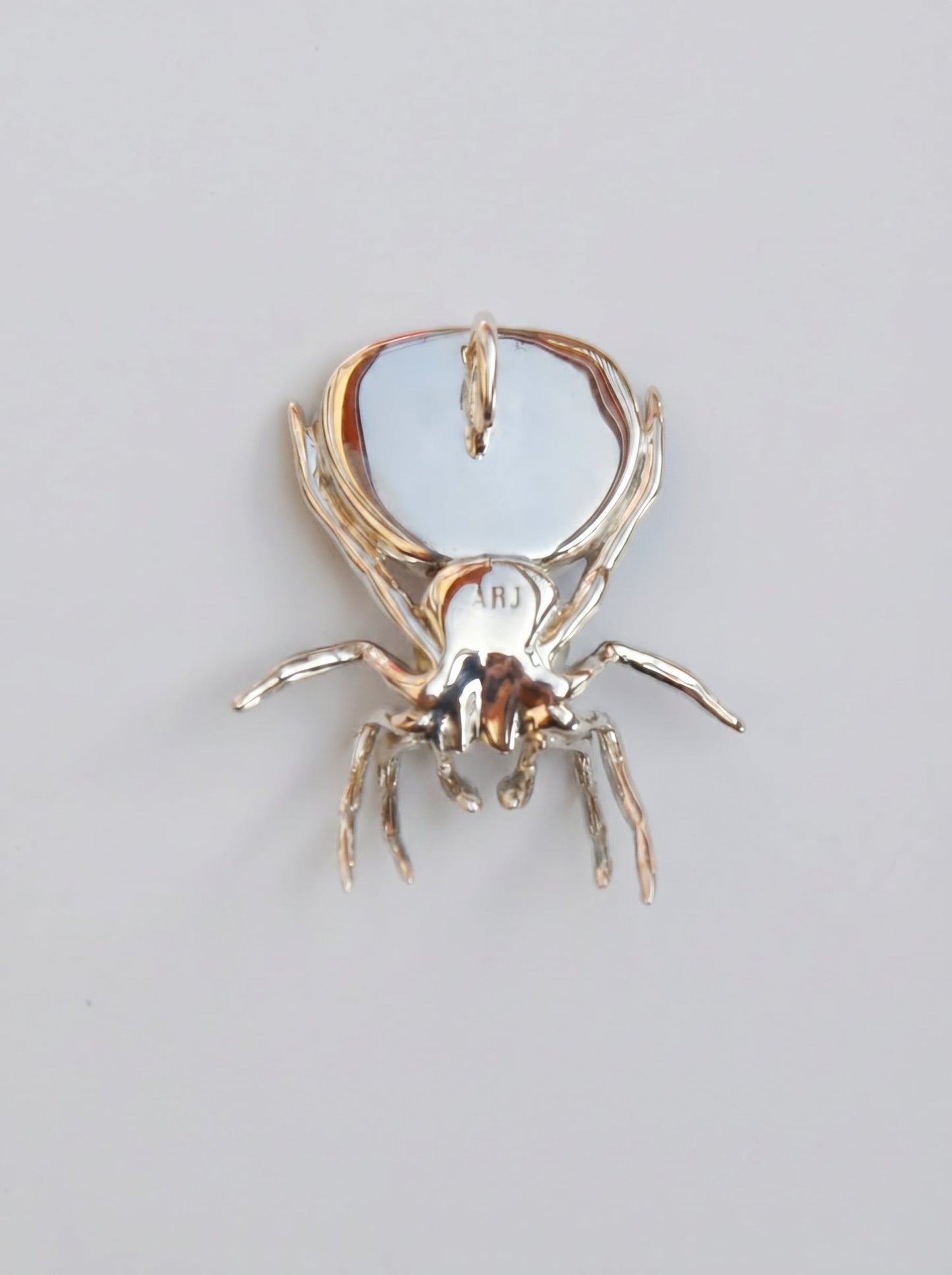 Back view of the peacock spider pendant showing the polished silver body and engraved detailing.