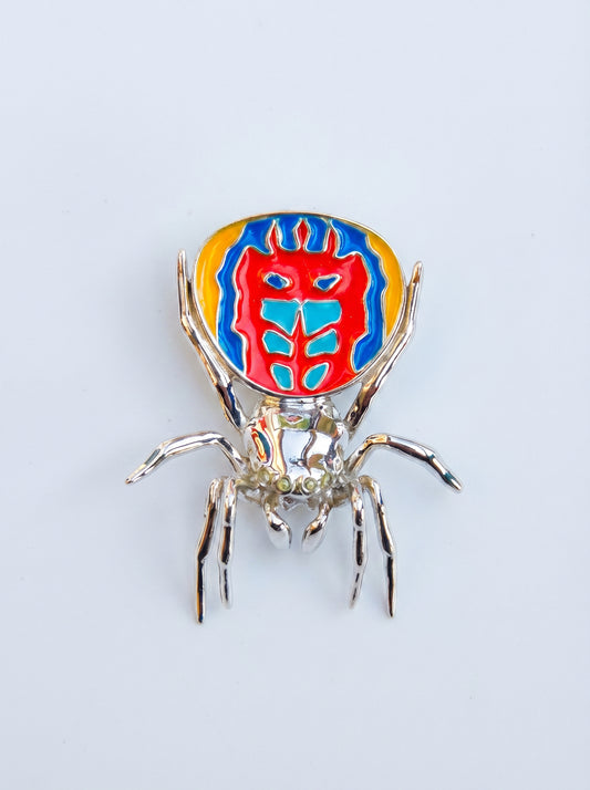 Peacock spider pendant with hand‑applied enamel and a mirror‑polished silver body shown on a white background.