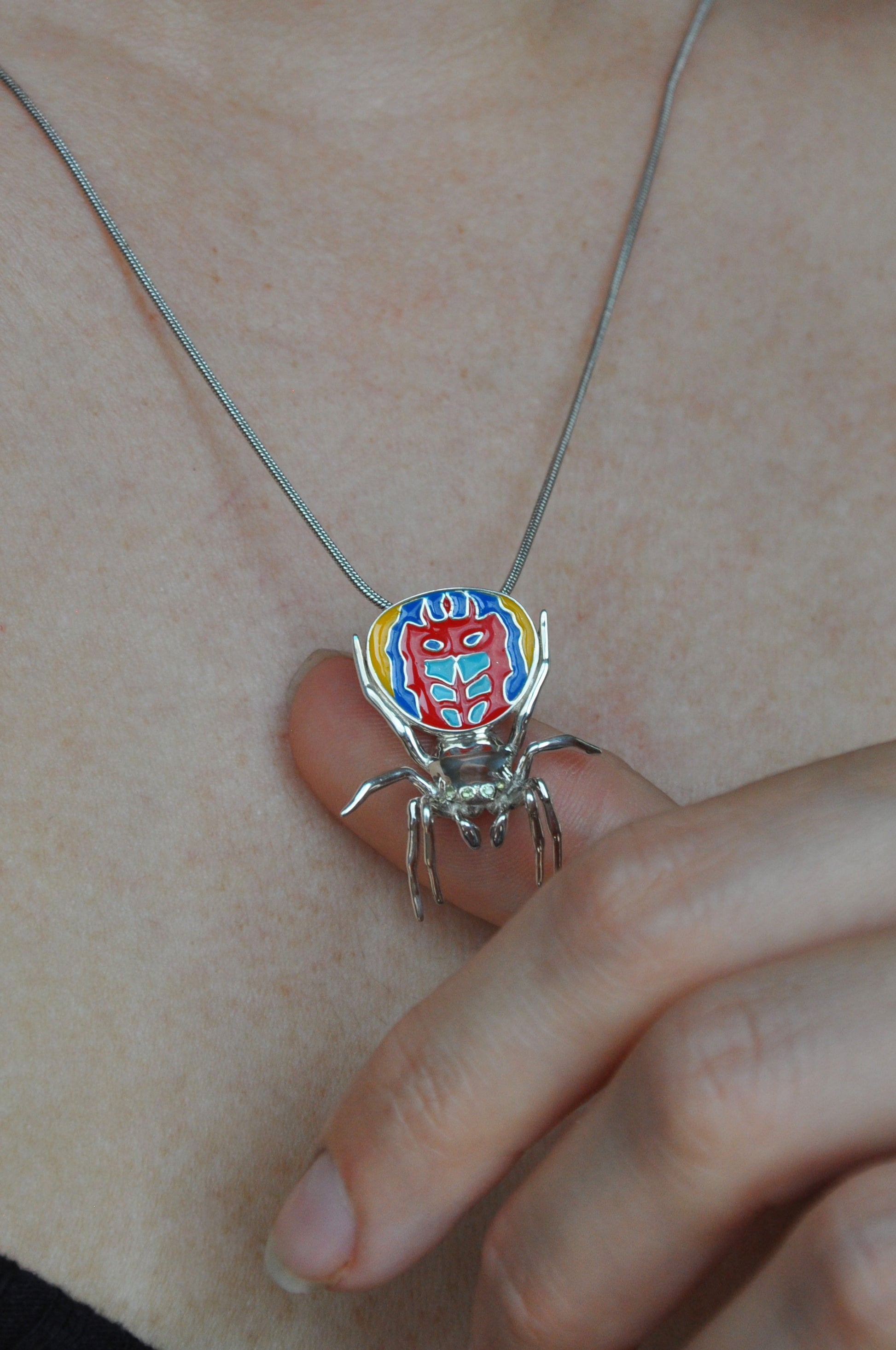 Peacock spider pendant worn on the neck, showing vibrant enamel colours and polished silver legs.